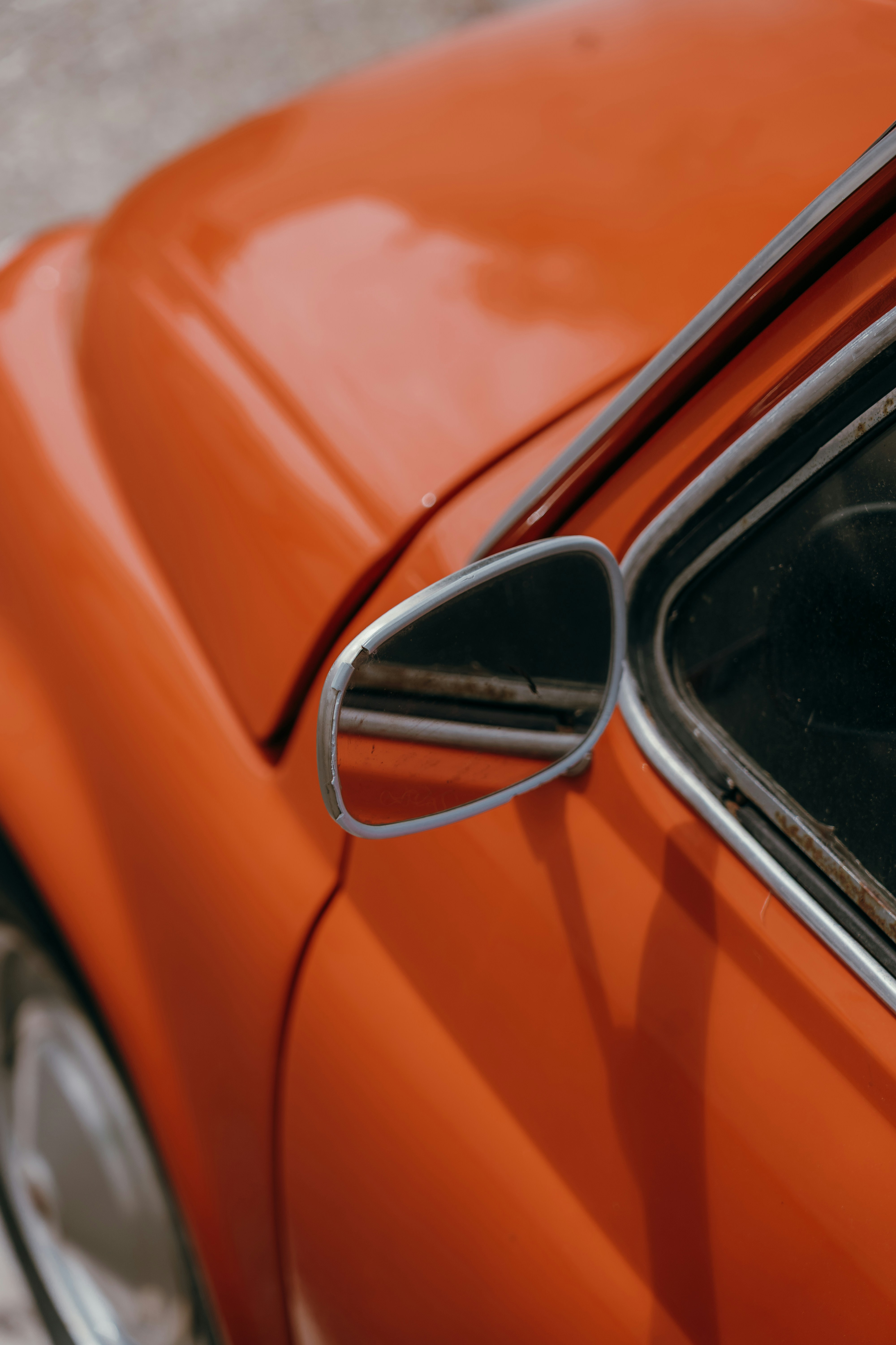 Side mirror reflecting a blurred background on an orange car