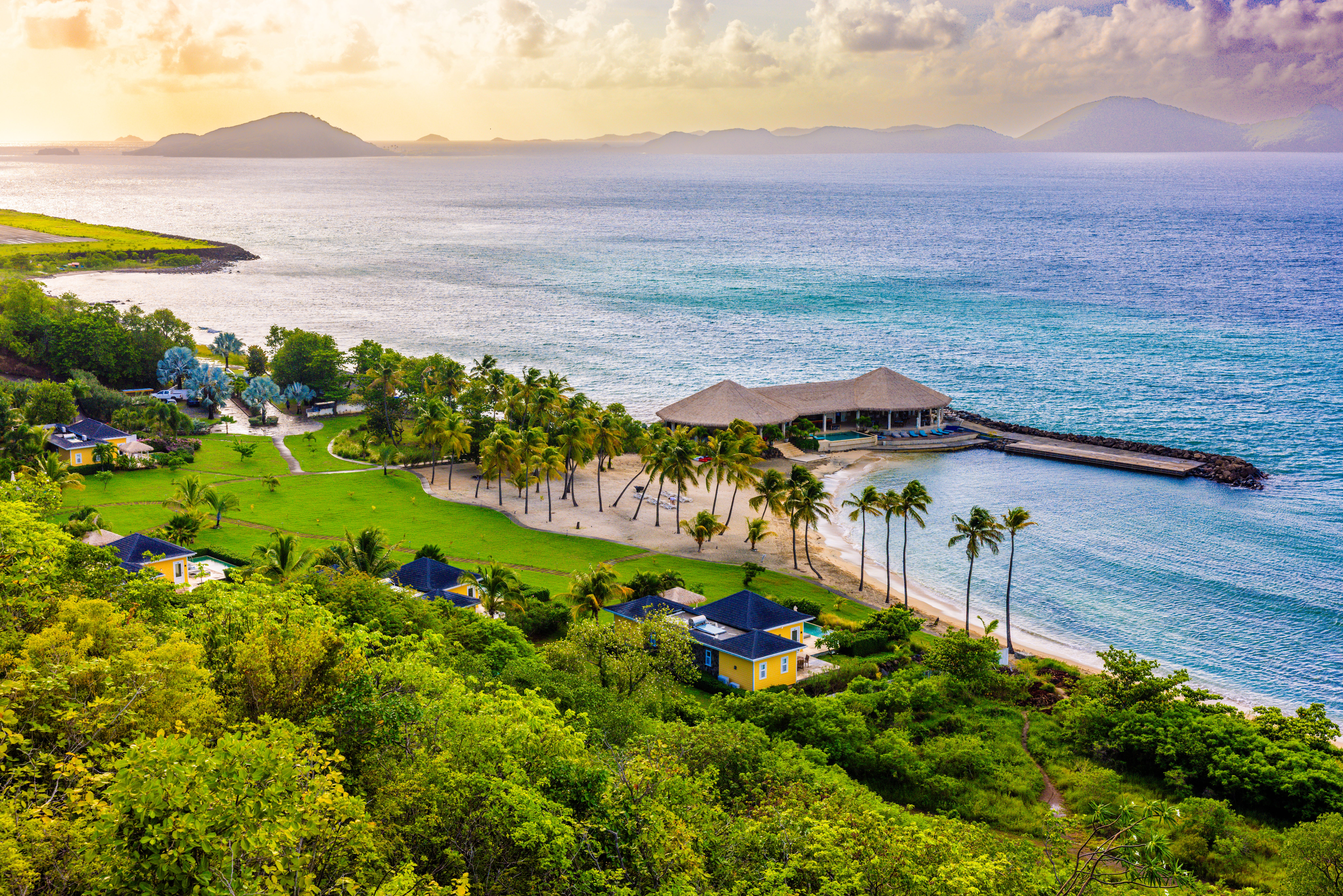 Aerial view of a lush coastal retreat with villas, palm trees, and turquoise ocean shoreline