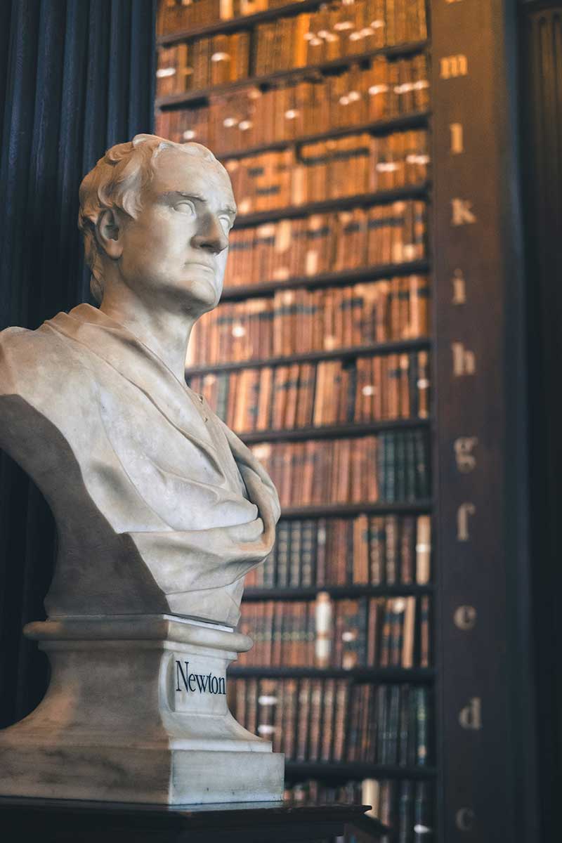Statue of Newton in a classic library setting, representing the principles of logic and reason that guide our legal services.
