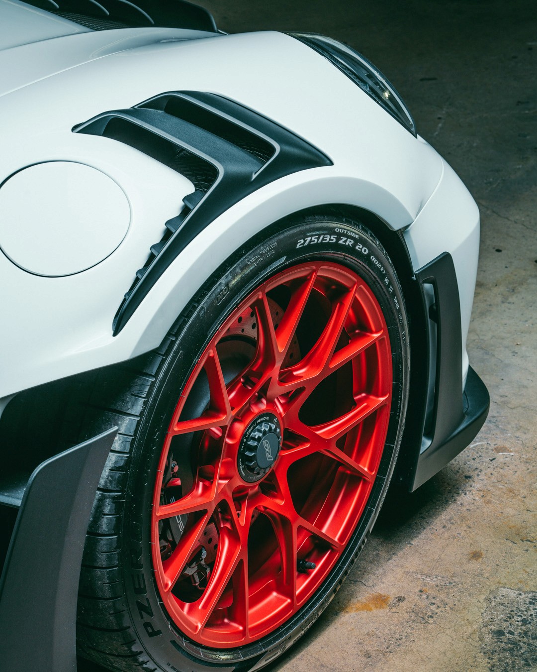 Close-up of a white Porsche 911 GT3 RS (992) front wheel, showing the red multi-spoke centre-lock rim, Pirelli P Zero 275/35 ZR20 tyre, carbon-fibre fender vents and front wing.