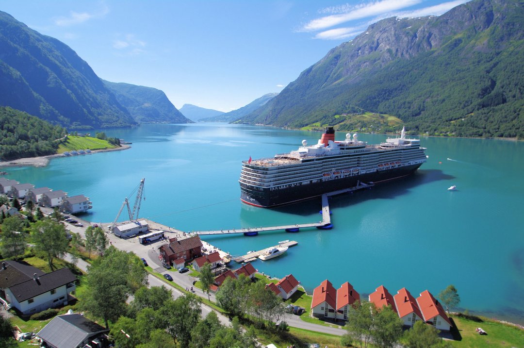 Cruise ship docked at a floating pier in Skjolden, Norway, connecting the vessel to shore amid calm fjord waters and surrounding mountains.
