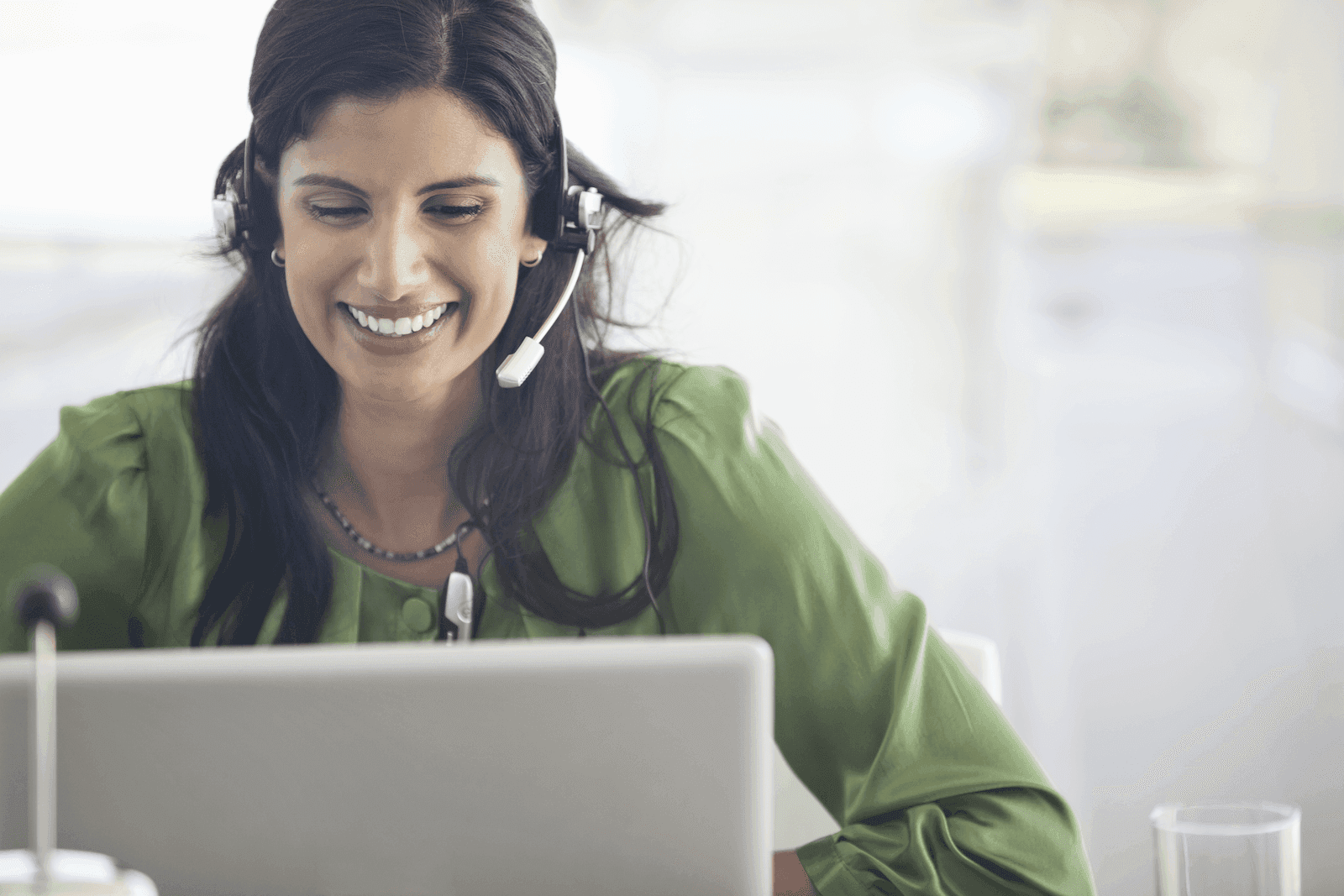 Woman wearing a headset and smiling while looking at her laptop