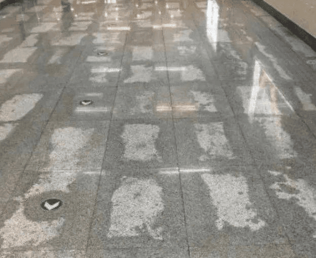 A stone floor showing visible white residue, indicating stone efflorescence on the polished surface.