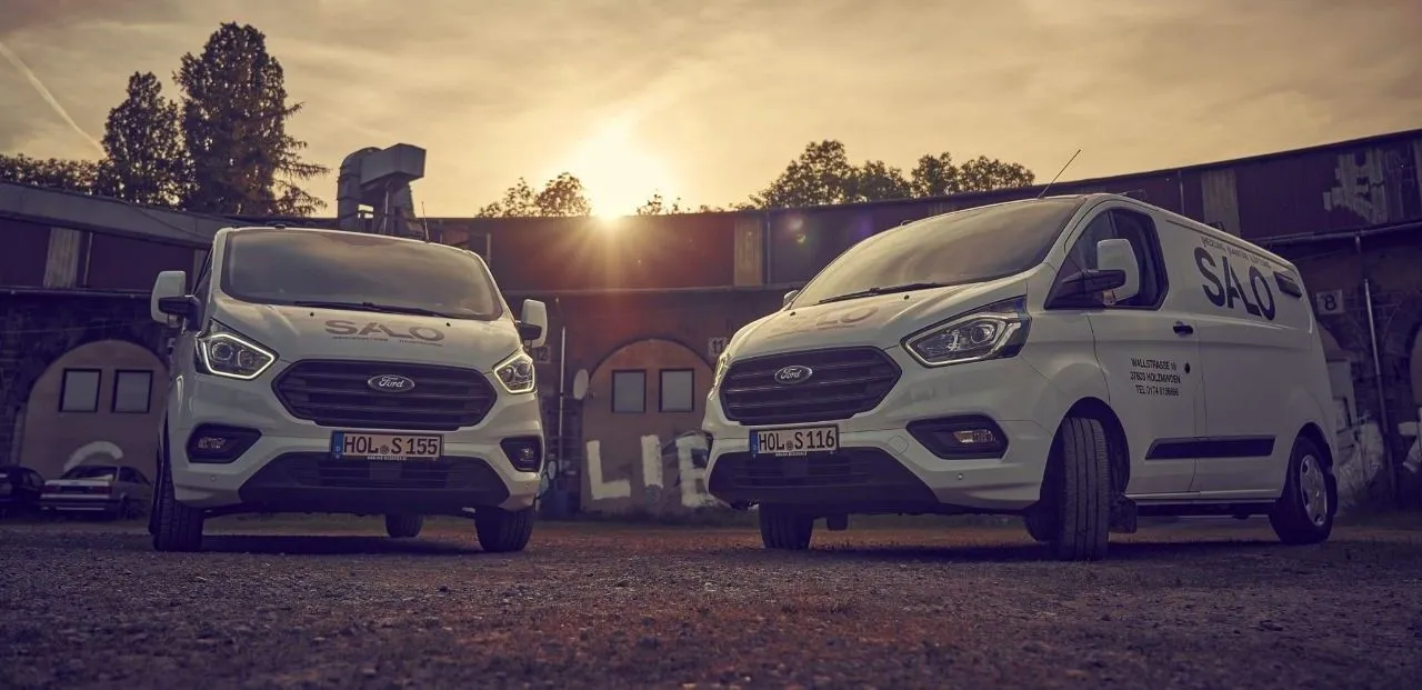 Drei Heizungsbauer sitzen auf einer Mauer vor einem Haus und erklären sich etwas.