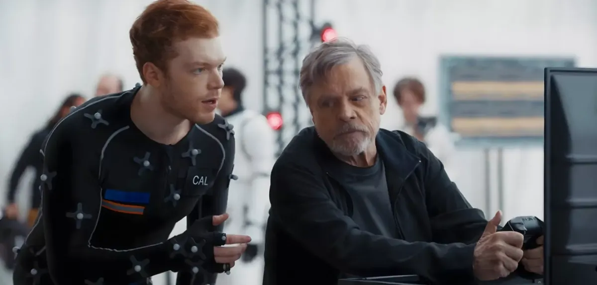 Cameron Monaghan in a motion capture suit standing next to Luke Skywalker actor Mark Hamill who is dressed in a black jacket and holding a video game controller