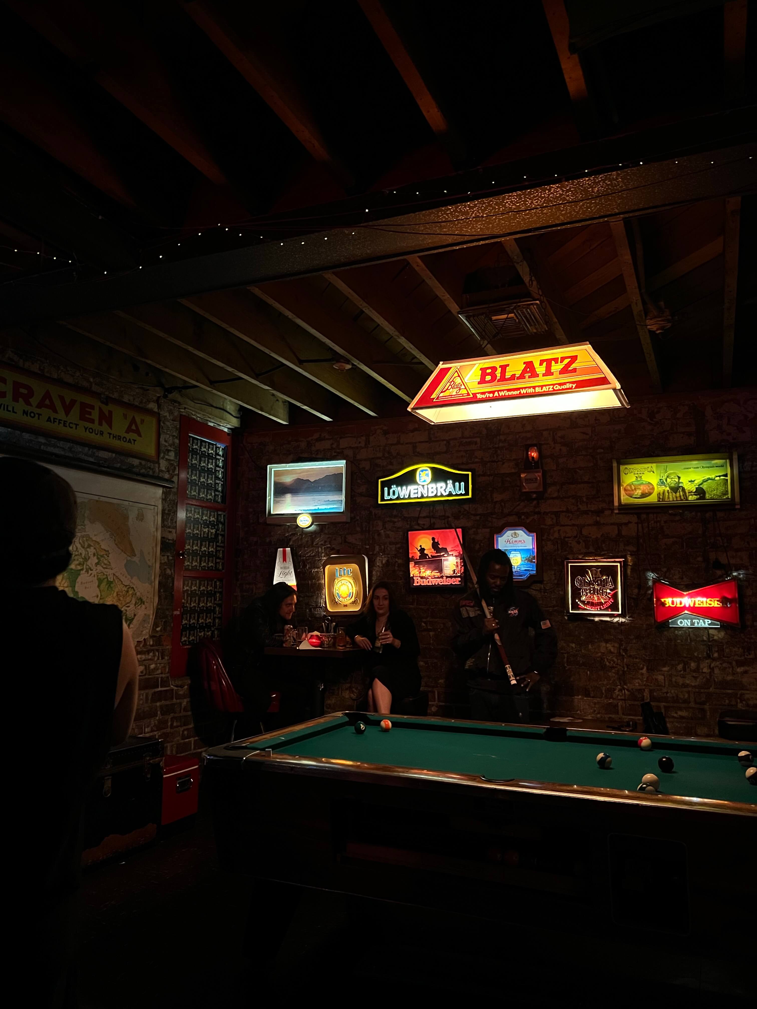 A dimly lit billiards bar with many tiffany lampshades hanging from the ceiling. 