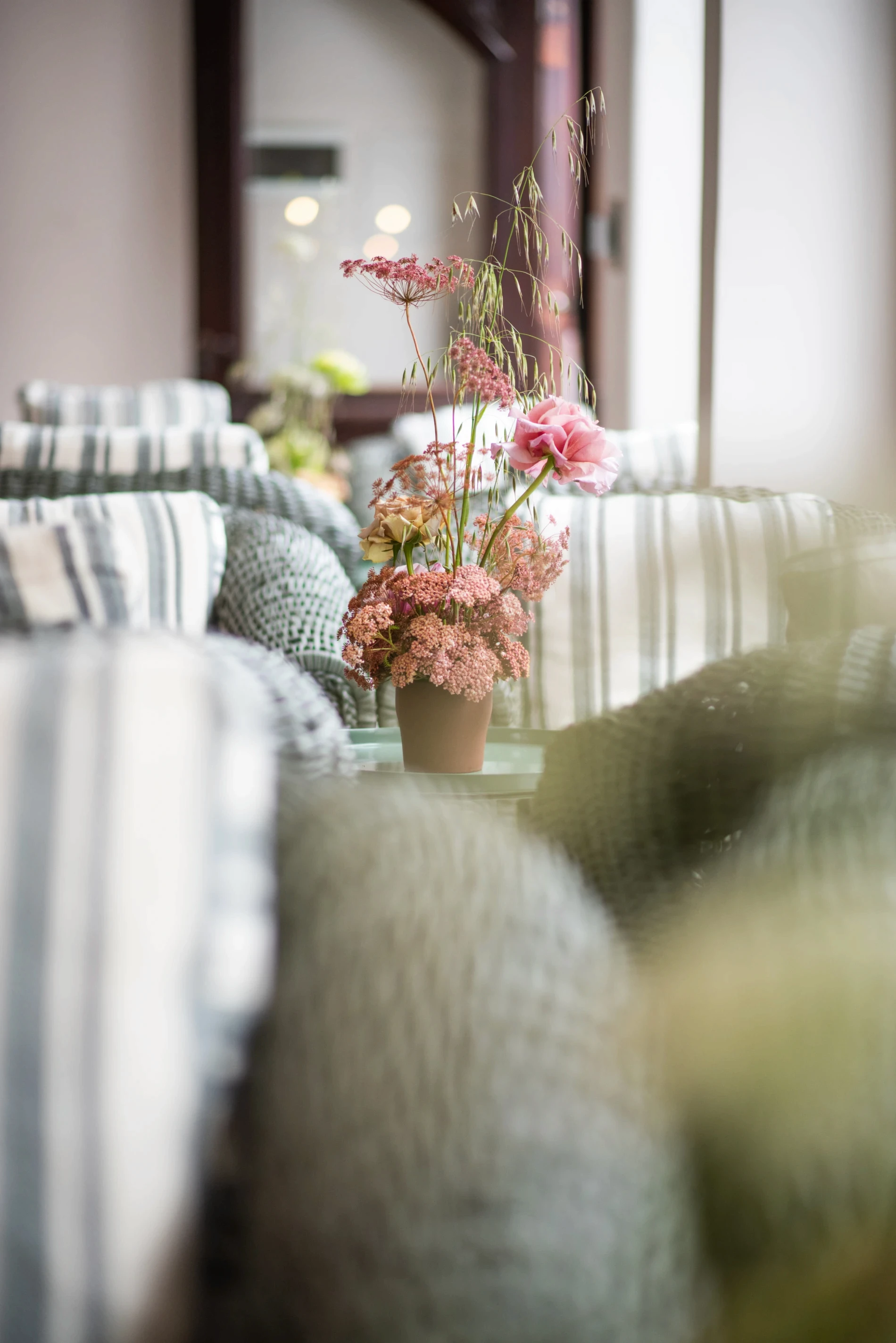 Arreglo floral delicado en tonos rosa viejo sobre mesa de apoyo en living con textiles a rayas en Villa María.