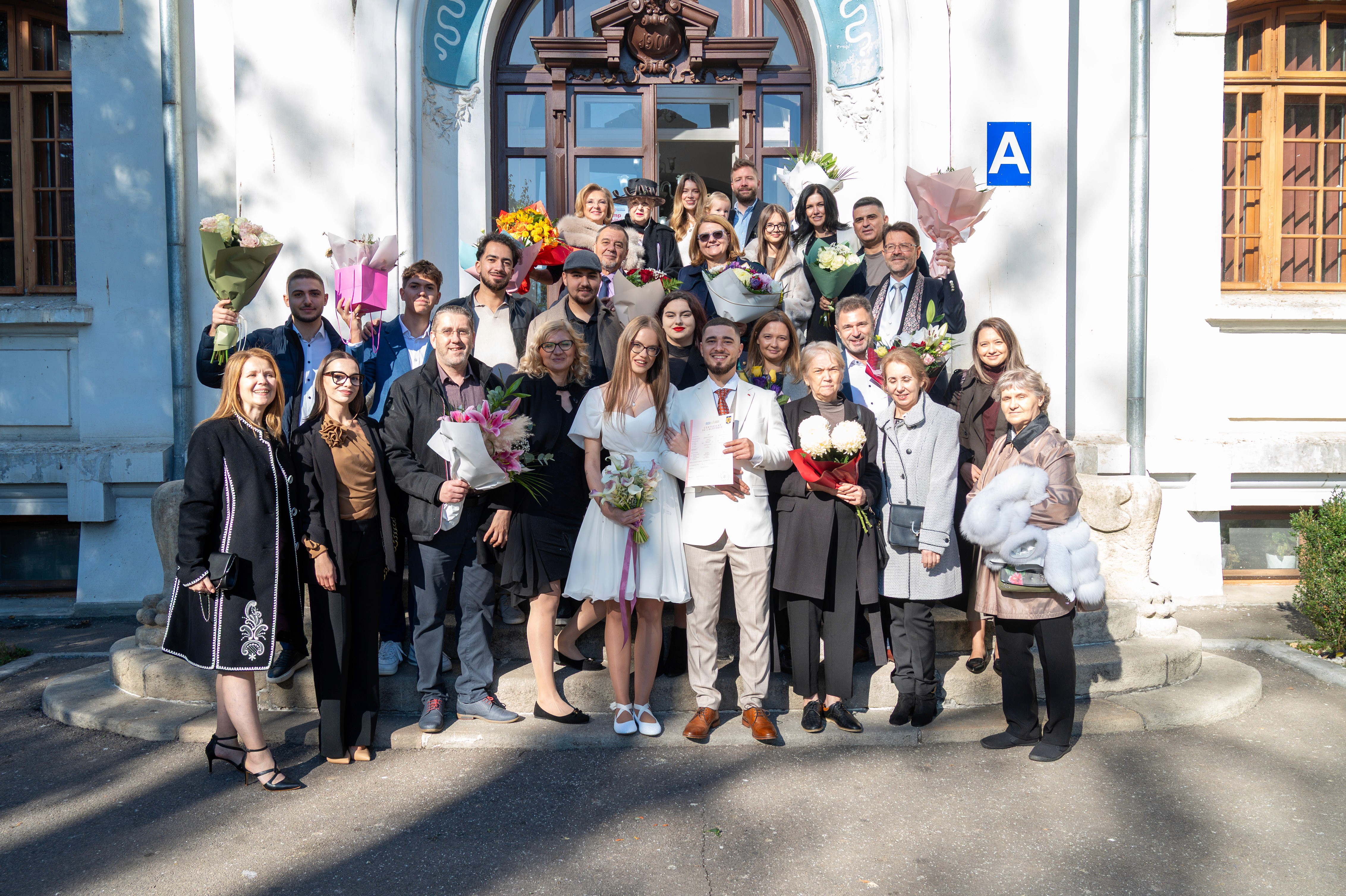 Fotografie de grup cu mirii și invitații după cununia civilă în fața Stării Civile sector 1 de sector din București.