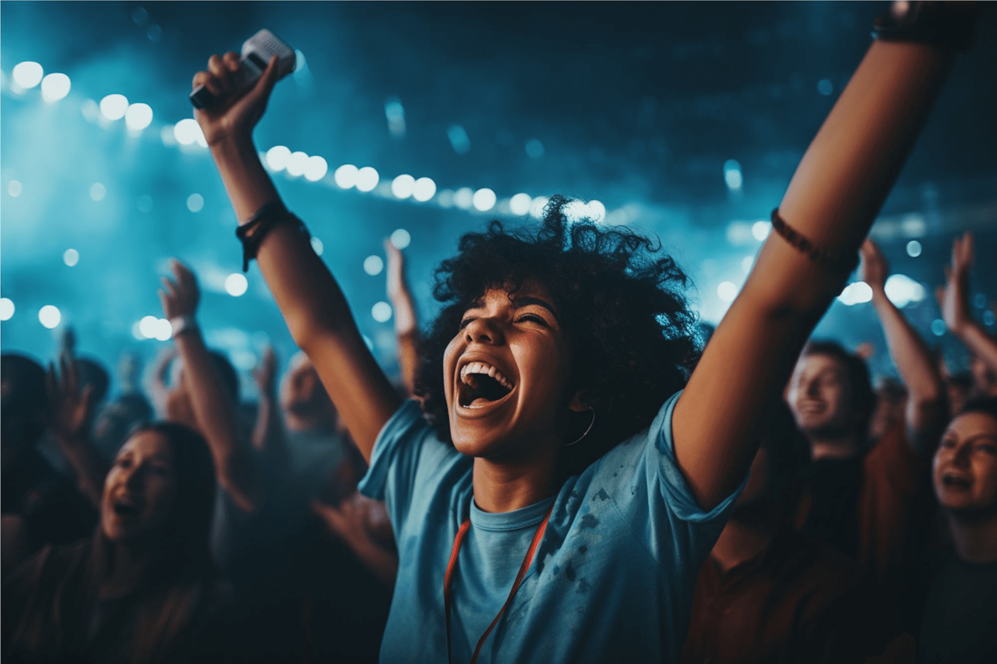 A joyful concert-goer with curly hair and a blue shirt ecstatically raises their arms in a crowded venue, illuminated by vibrant stage lights, capturing the thrilling atmosphere of a live music event.