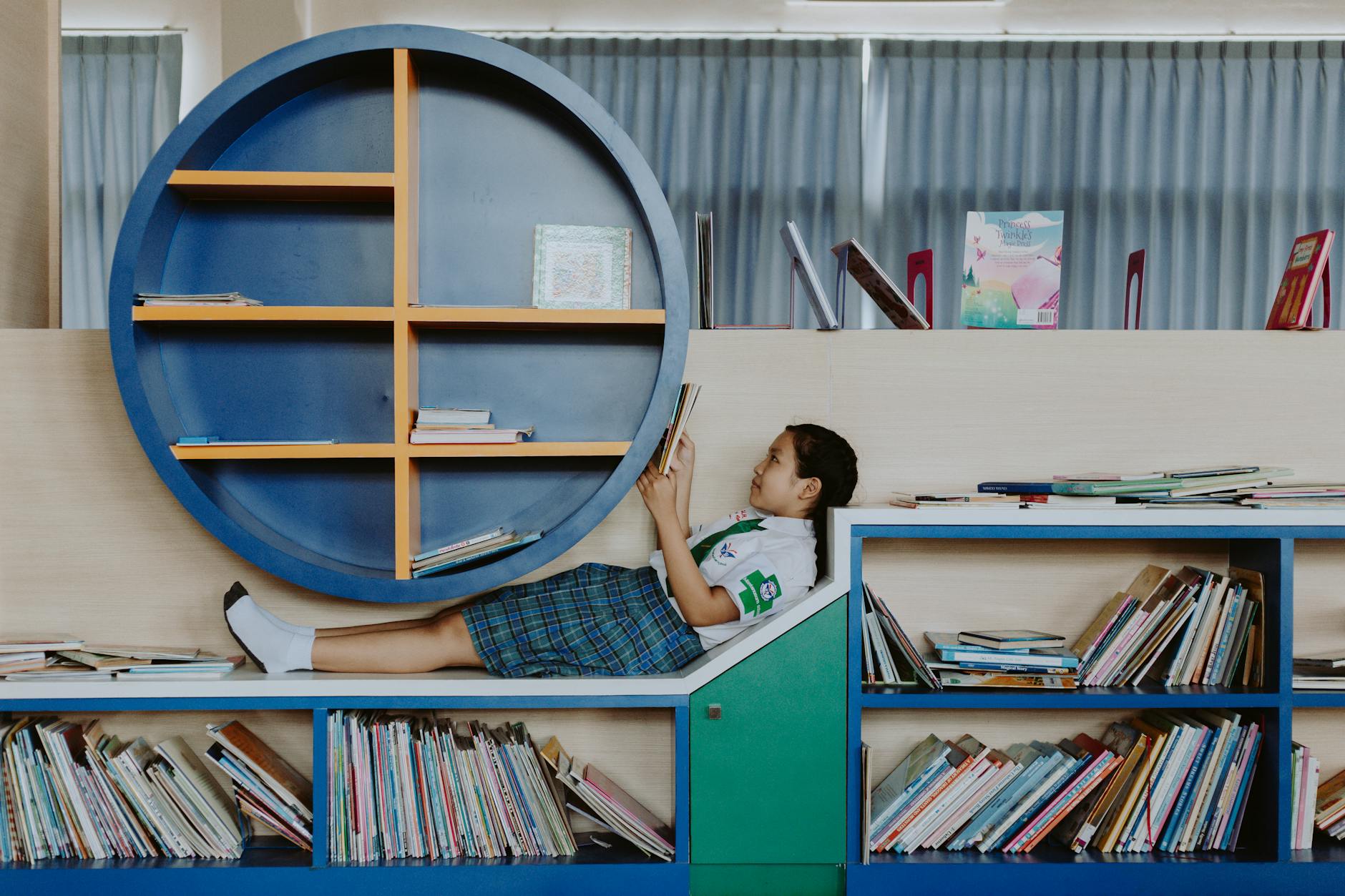 A young elementary student sitting in a cozy library nook holding a thick chapter book with a bright cover.