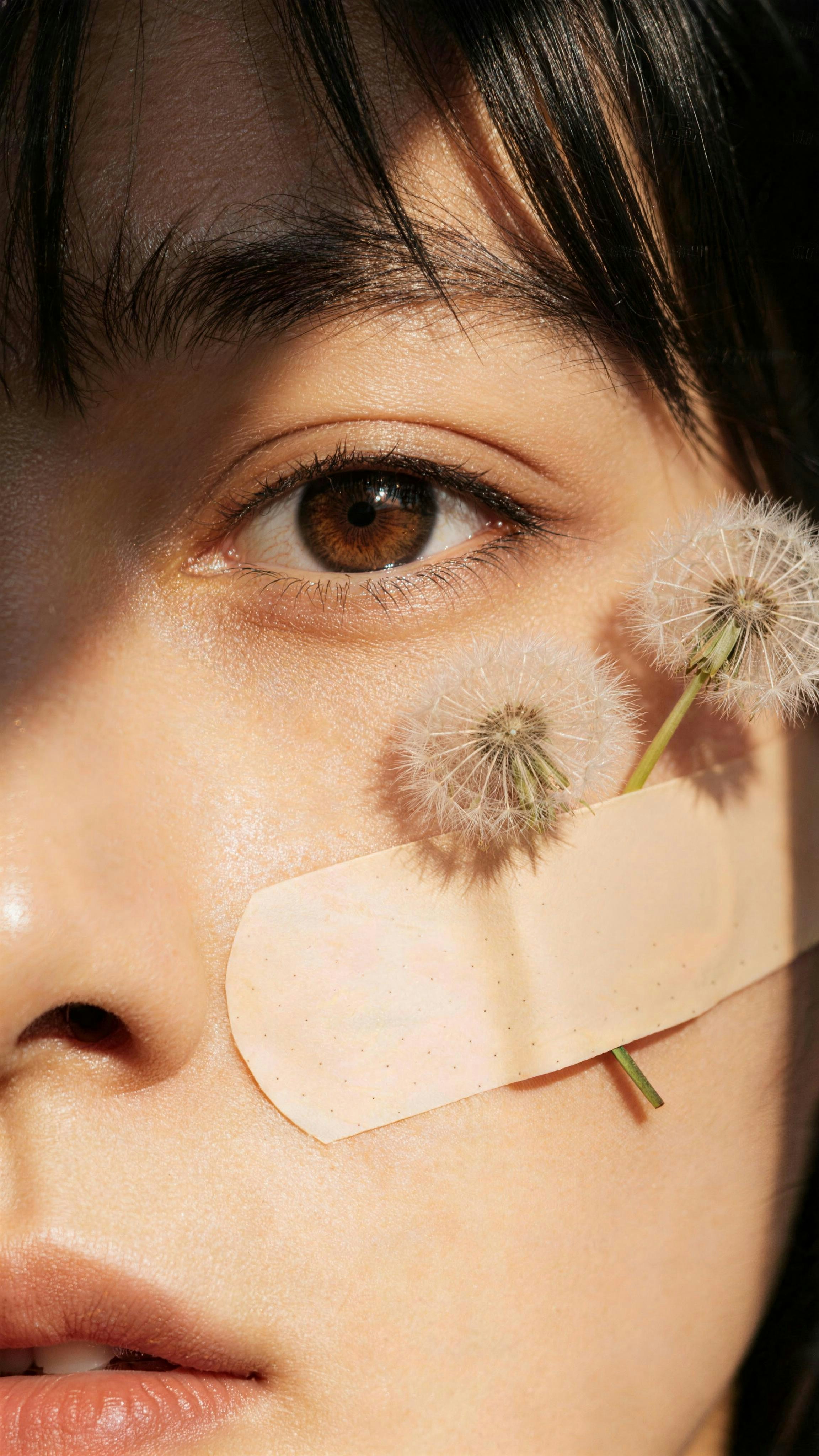 Close-up of a woman's face with dandelions and bandage.