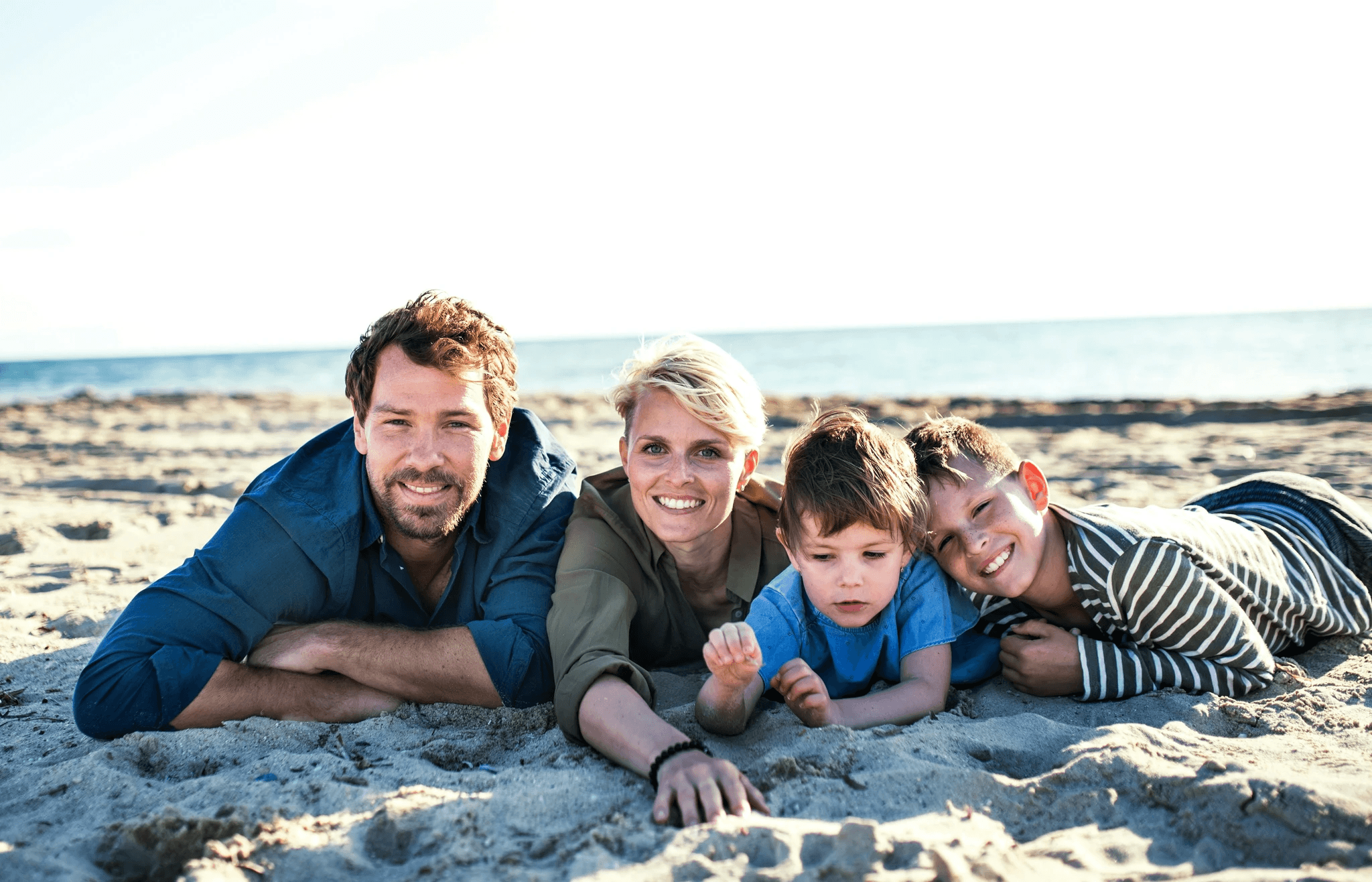 two adults and children lying in sand on a beach