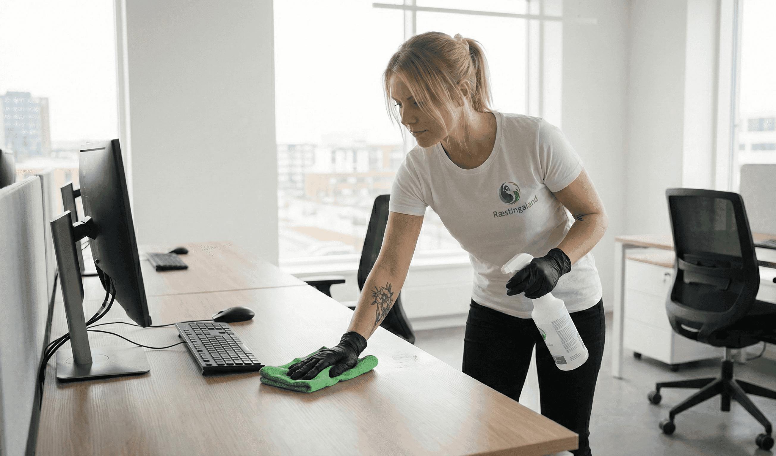 Starfsmaður Ræstingaland að þurrka af skrifborði og vinnusvæði á skrifstofu.