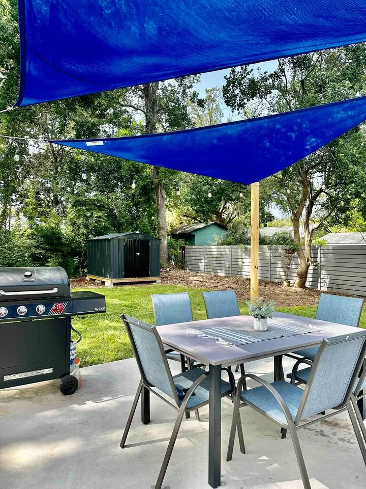 Patio dining table for six under blue sail shades beside the gas grill