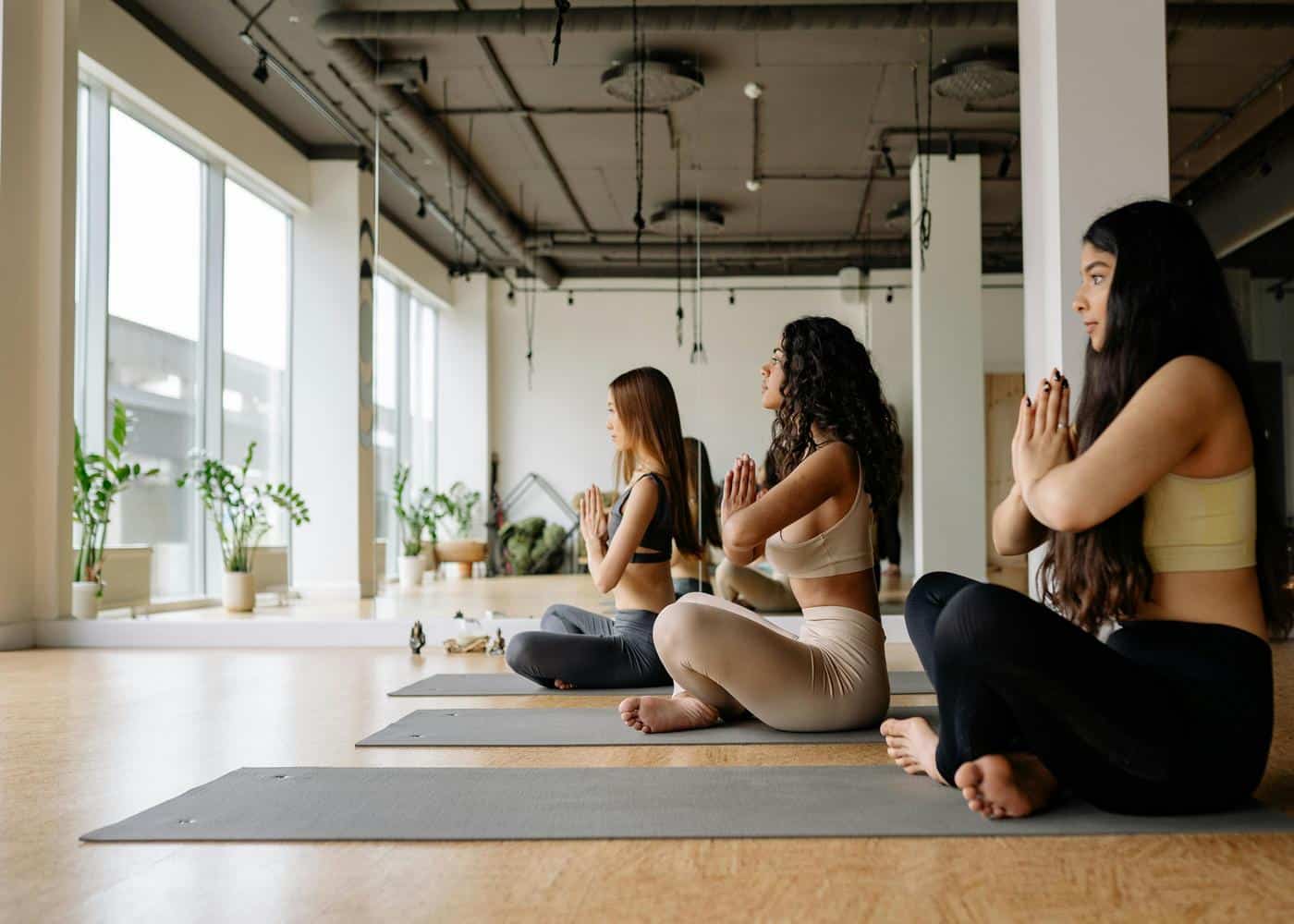 Three women indoors meditating on yoga mats to showcase health and wellness trends