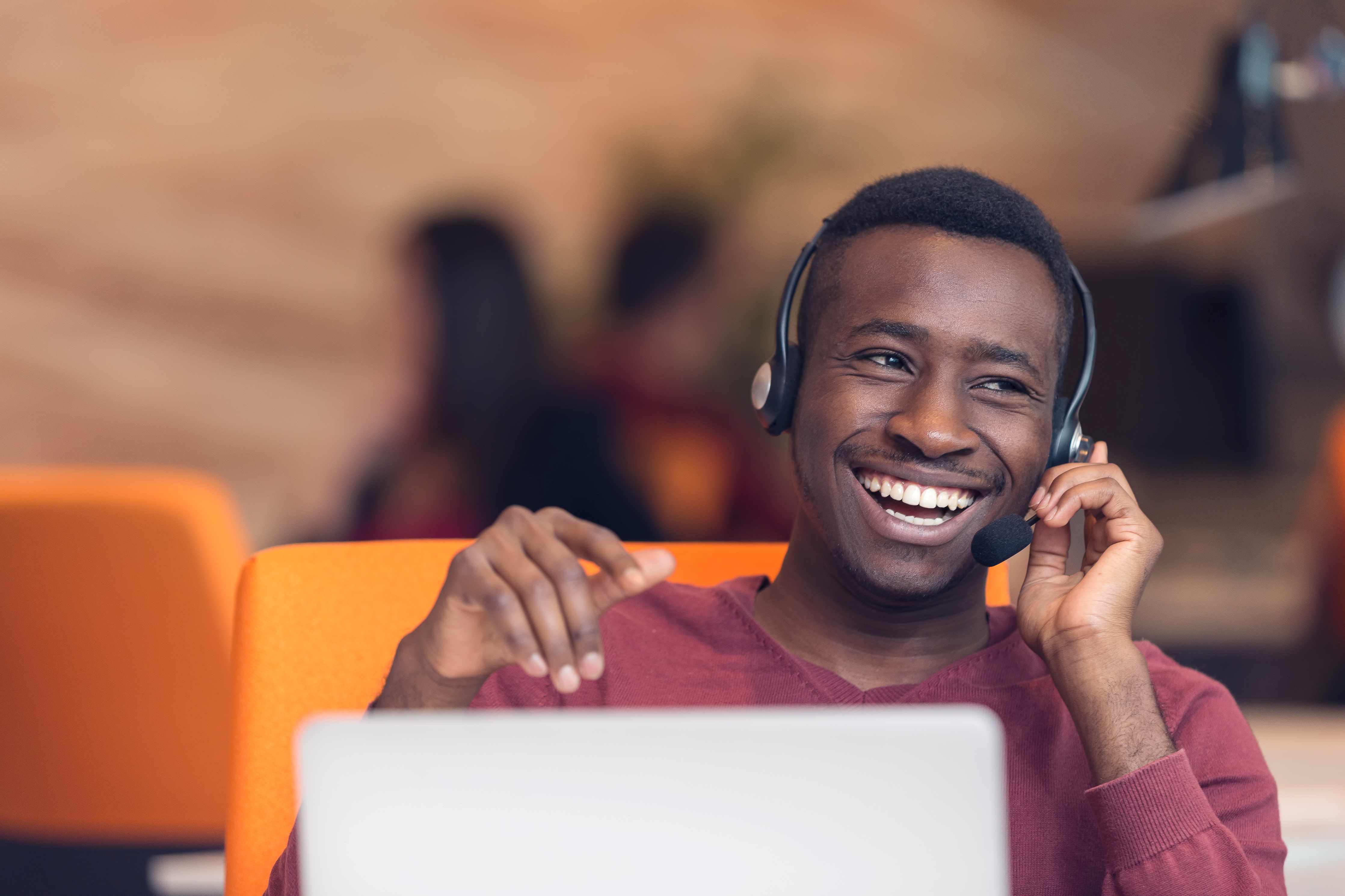 Customer service representative smiling while using a headset at a computer.
