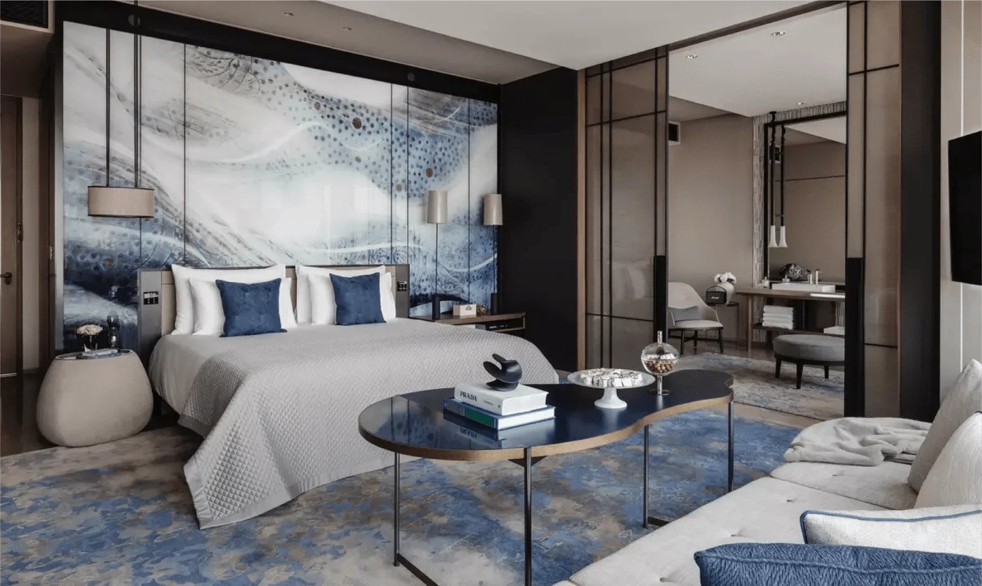 غرفة نوم عصرية بديكور أزرق وأبيض تضم سريرًا وطاولة جانبية وأعمال فنية بسيطة، تعكس أناقة التصميم في مشروع ون زعبيل.