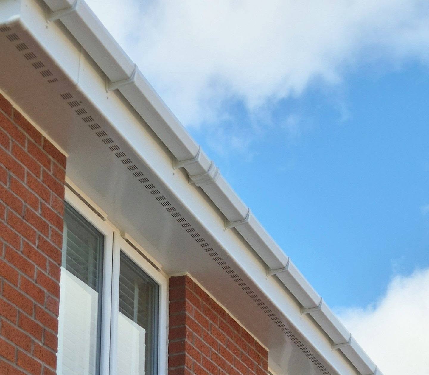Red brick building corner with a white soffit and guttering against a bright blue sky.