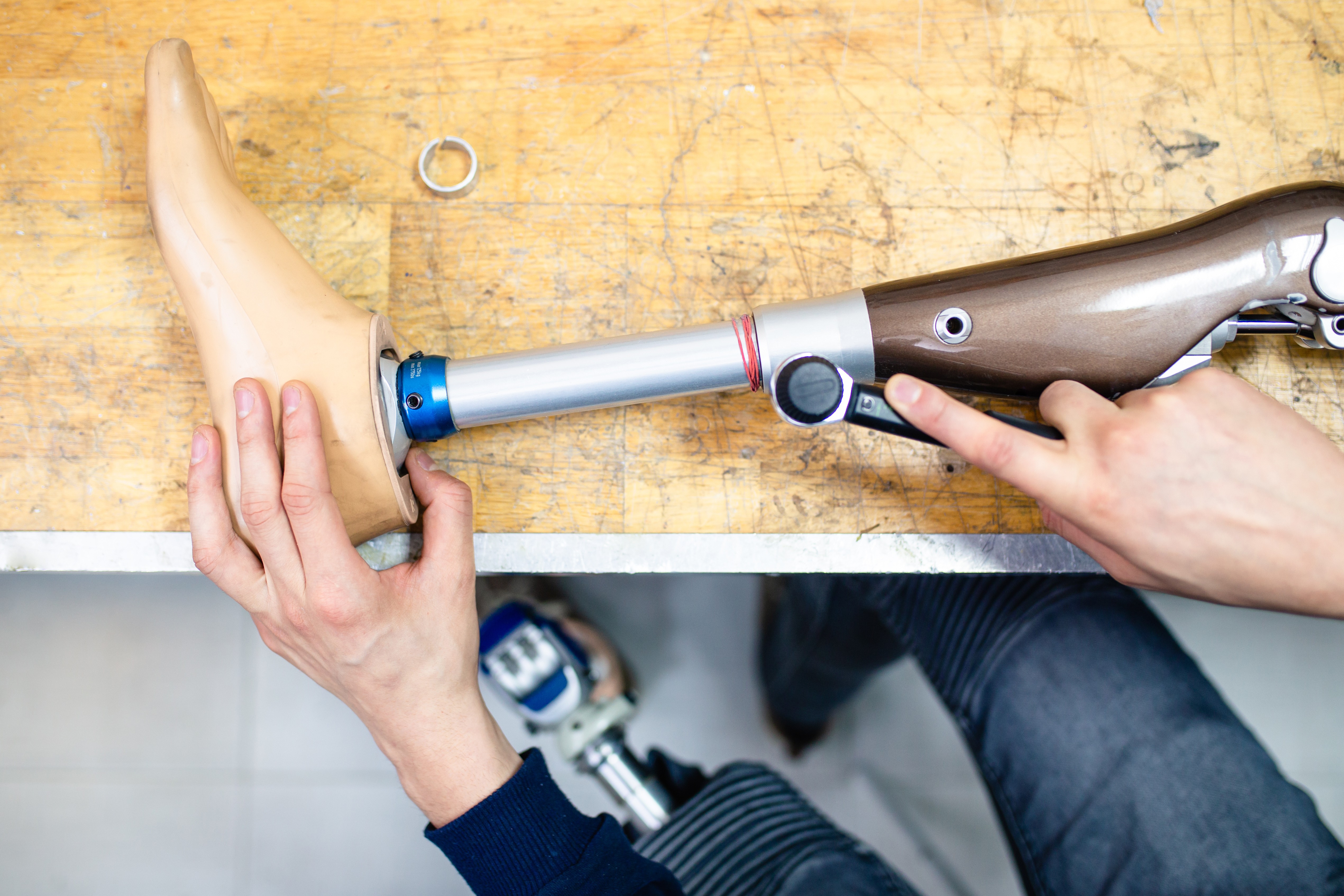 Overhead view of a technician's hands adjusting a prosthetic leg with a torque wrench on a wooden workbench