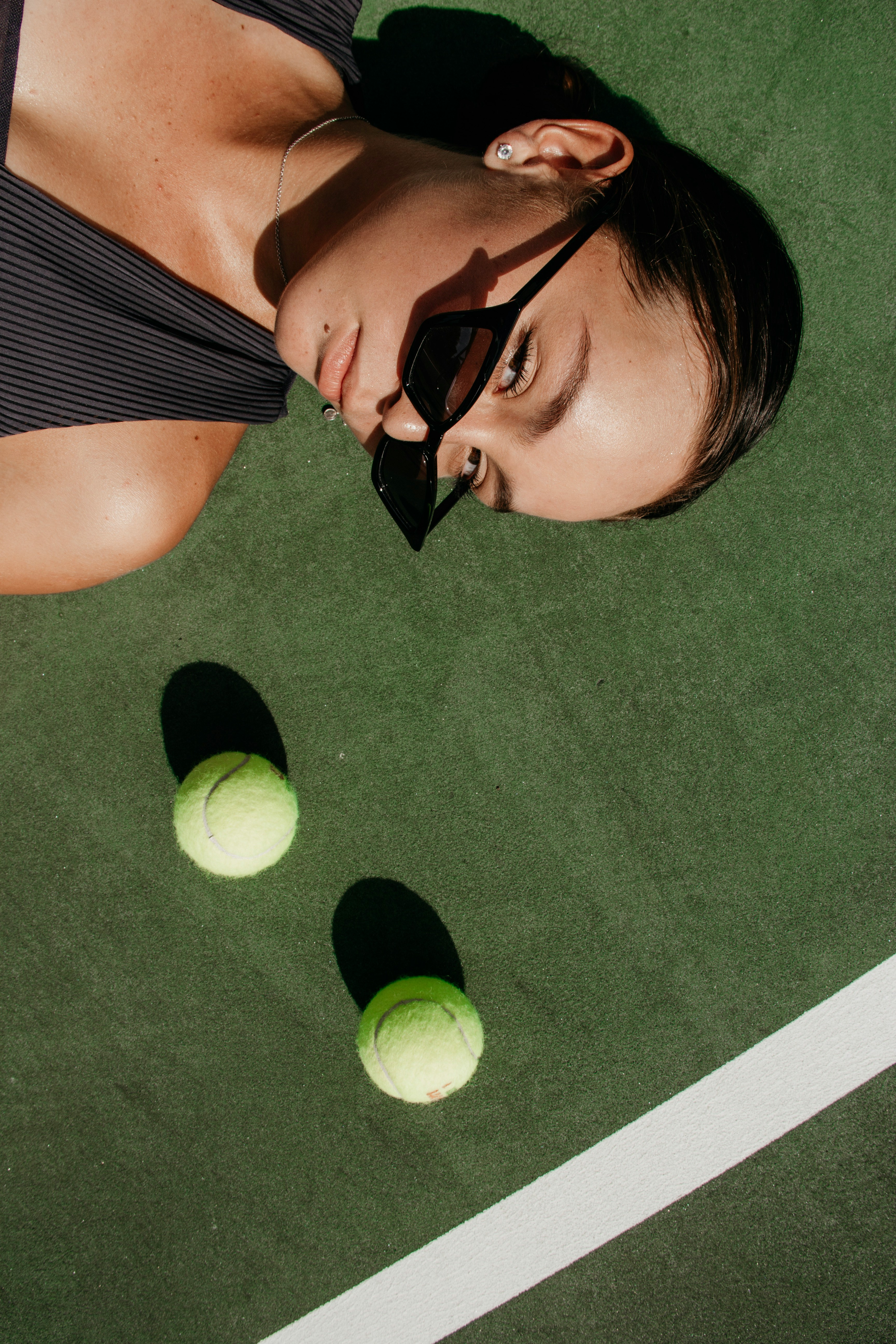 Mujer  con gafas de sol oscuras y vestido oscuro acostada de lado sobre una cancha de tenis.