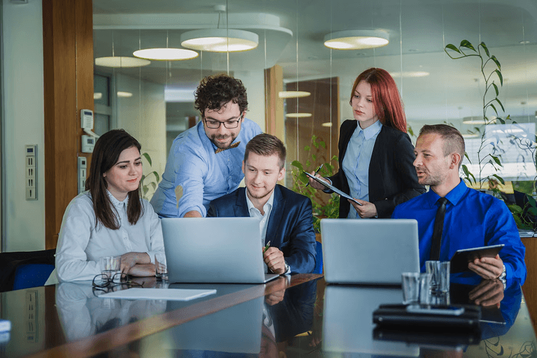 Cross-functional development team collaborating around laptops in a meeting room, representing a managed development team delivering end-to-end ownership beyond staff augmentation.