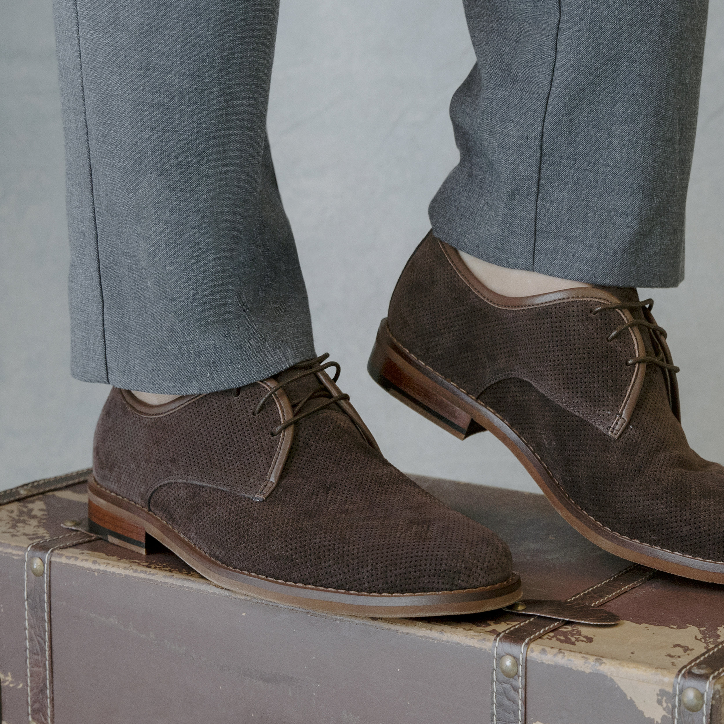 Close-up of Florsheim brown suede shoes on a vintage suitcase, showcasing their textured material and classic design.