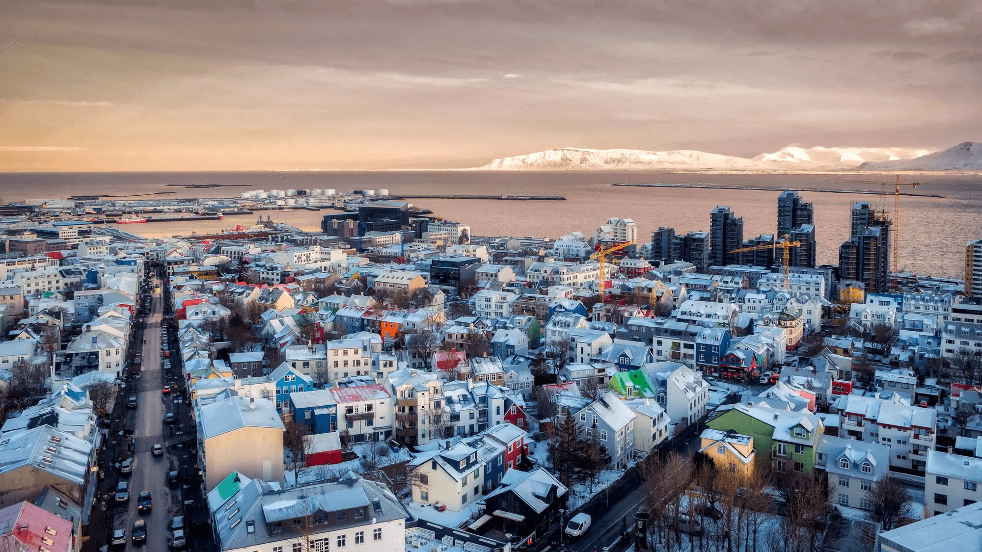 Aerial view of snowy Reykjavík rooftops and the bay at dusk