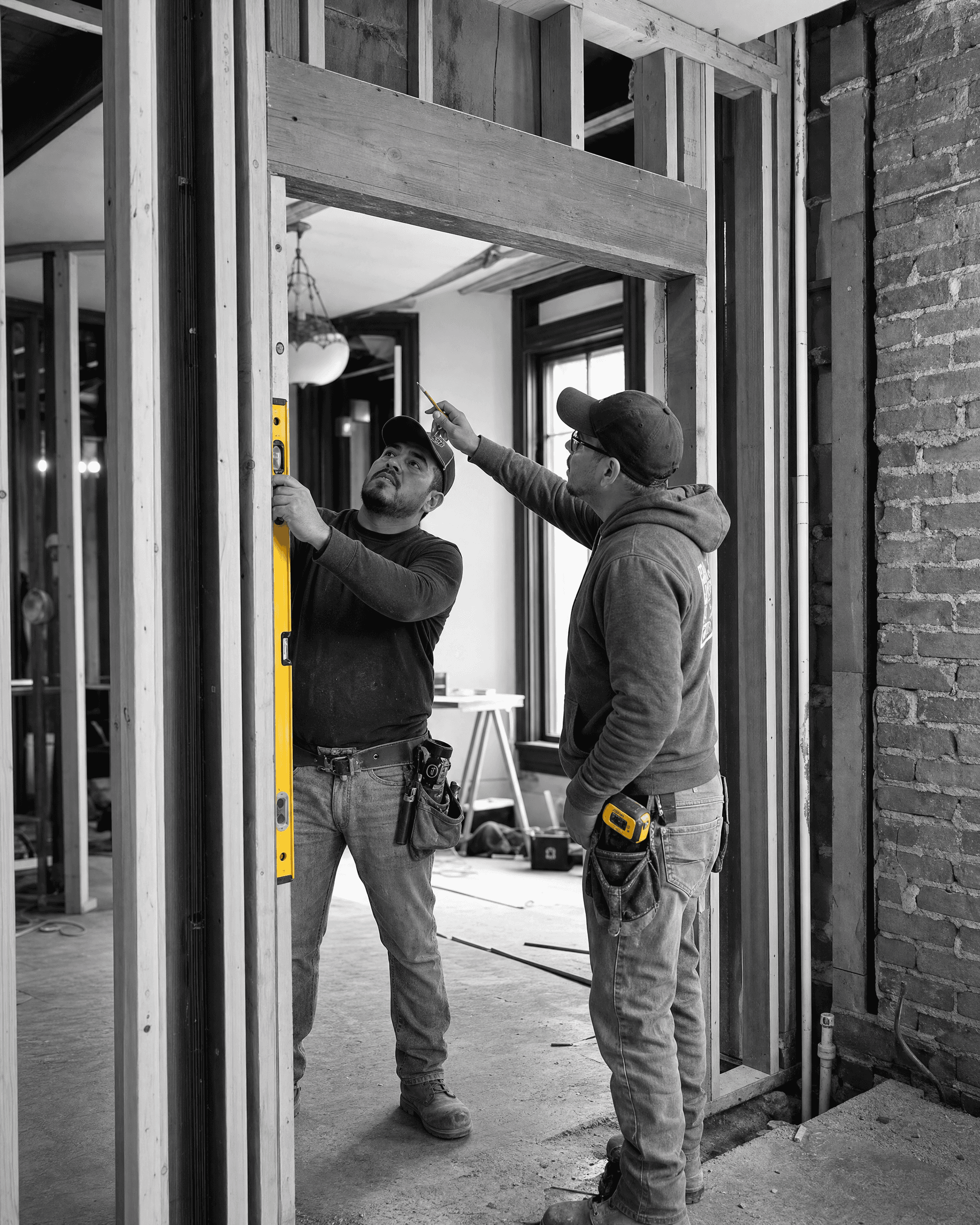 Two construction professionals checking a framed opening with a level during an active home renovation.