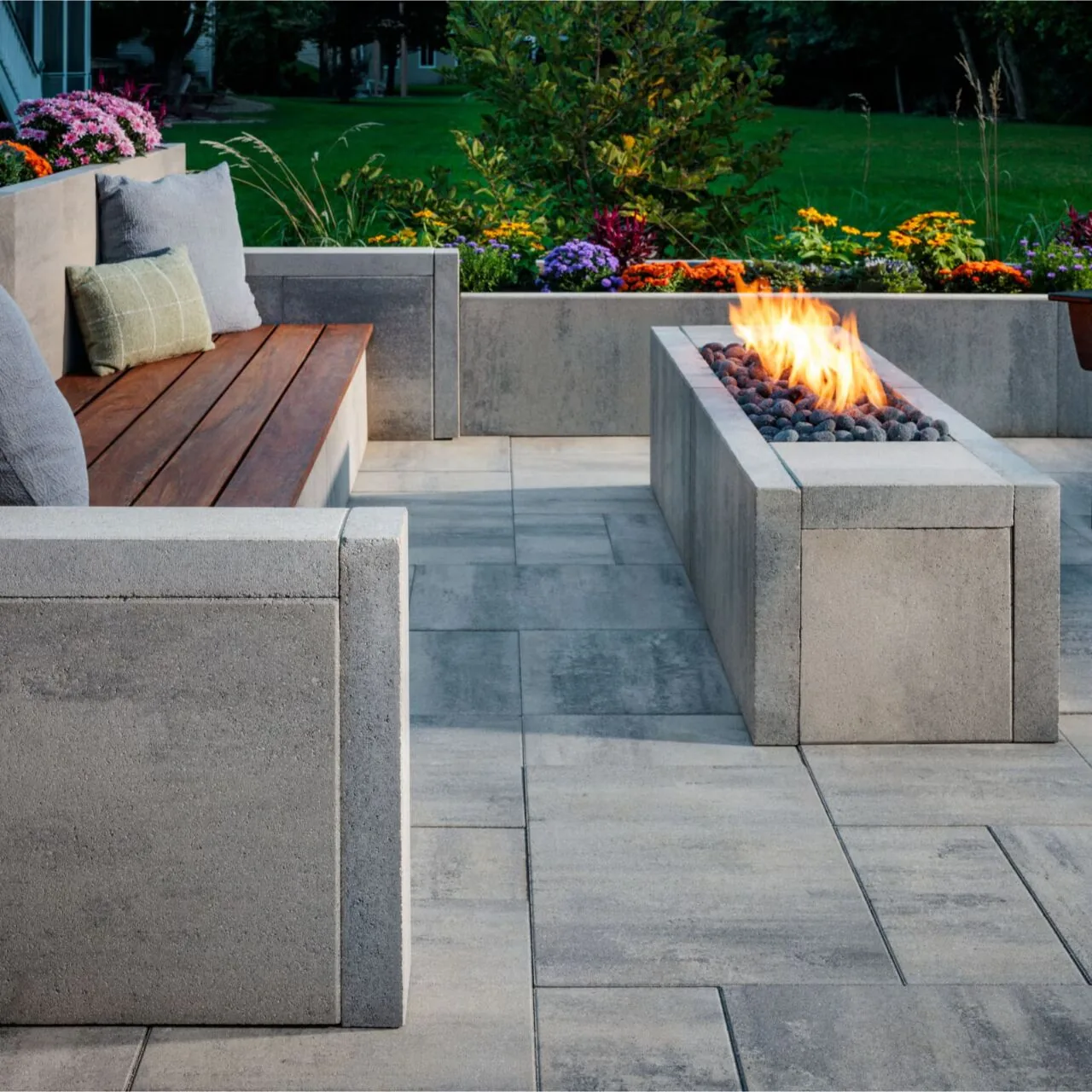 A quiet modern terrace Large gray paving slabs beside a rectangular fire feature and built-in timber seating.