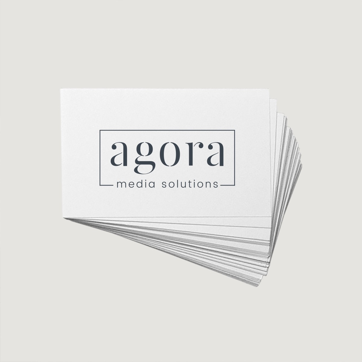 AGORA Media Solutions logo on a stack of white business cards featuring minimalist typography and modern branding.