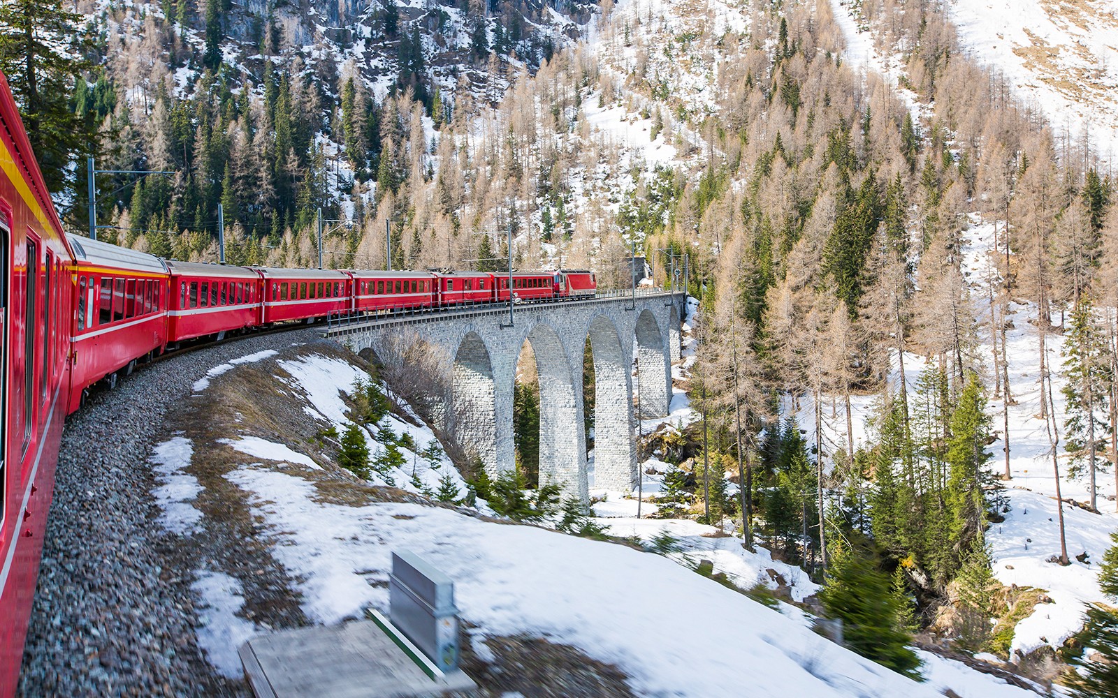 Karlarla kaplı Alpler'in manzarası eşliğinde taş bir viyadükten geçen Bernina treni.