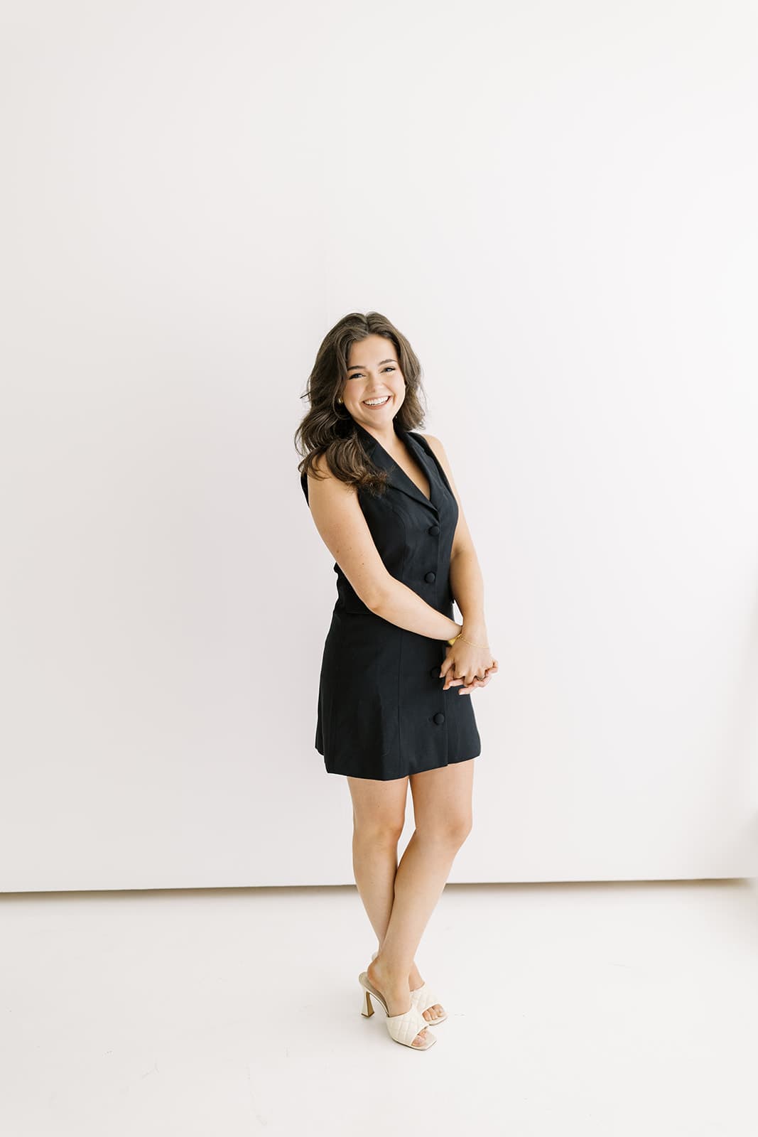 A model in a black dress smiles while standing in the bright, minimalist setting of Revelator Studio in Shreveport, captured by photographer Andy Roberts, showcasing the studio’s natural light and clean aesthetic.