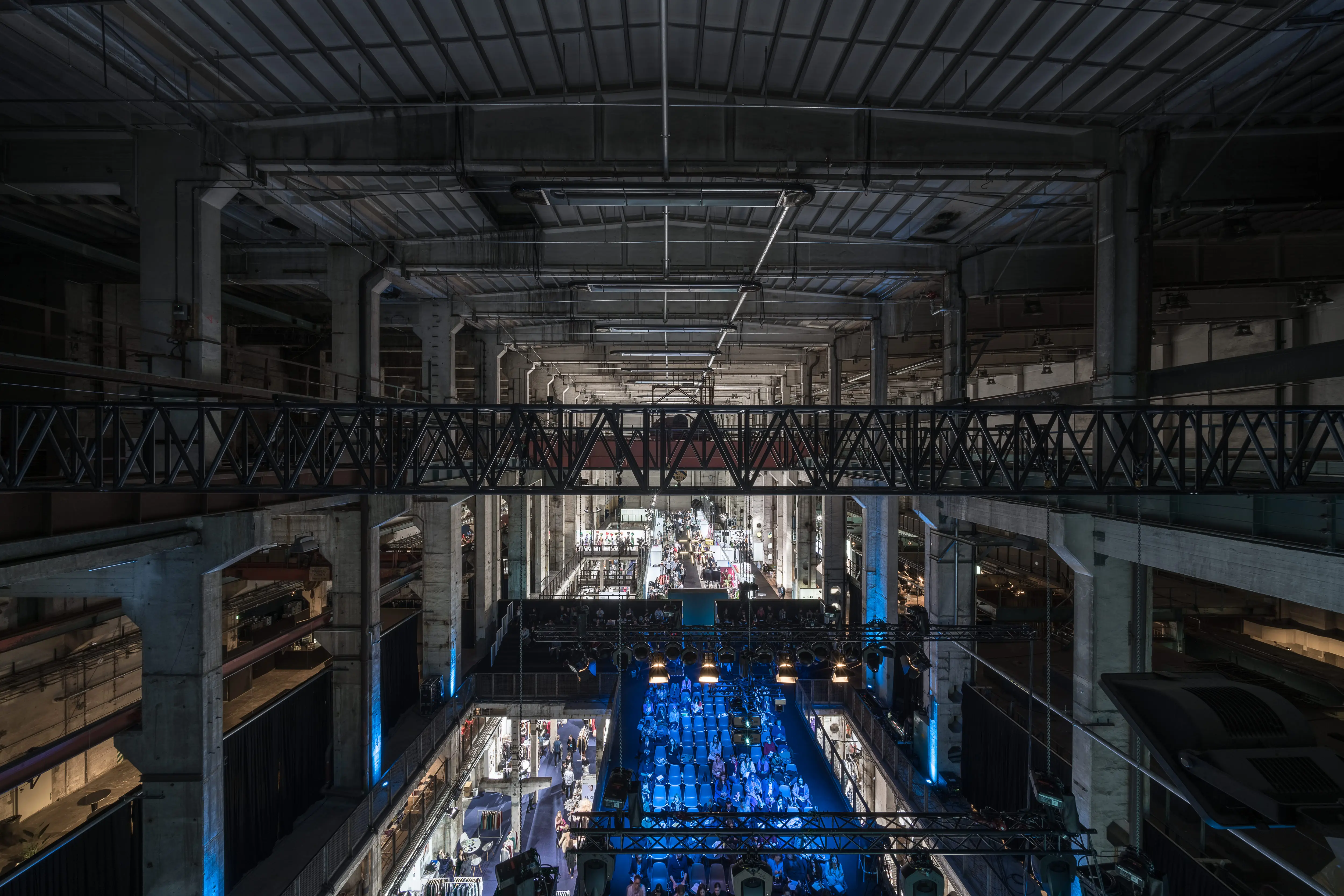 Vast concrete hall of Kraftwerk Berlin with steel trusses, the blue-lit NEONYT conference area glowing on the lower level.