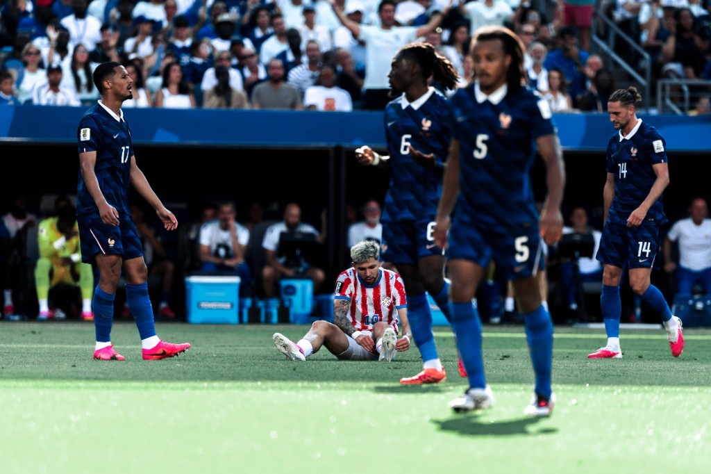A Paraguay player sits on the grass adjusting his boot while French teammates walk past during their World Cup clash