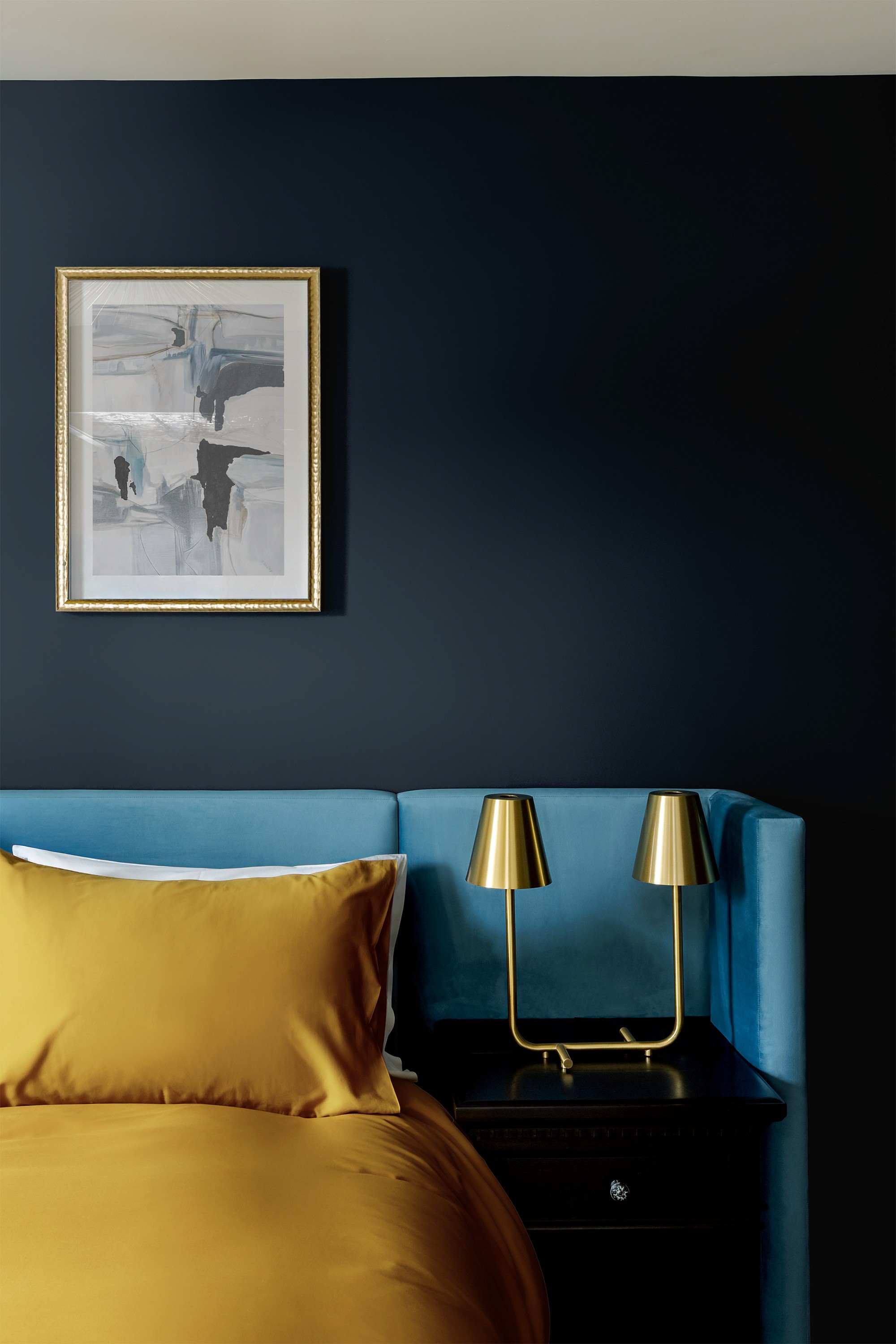 Hattan House bedside detail, blue velvet headboard with mustard linens beneath twin brass task lamps and framed abstract artwork