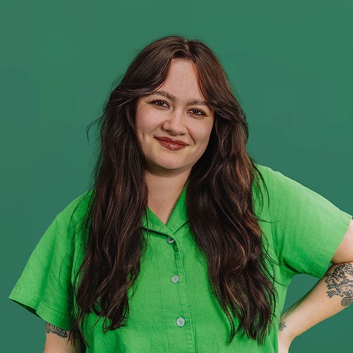 Woman with long dark hair wearing a green short-sleeve shirt, smiling gently against a green background.