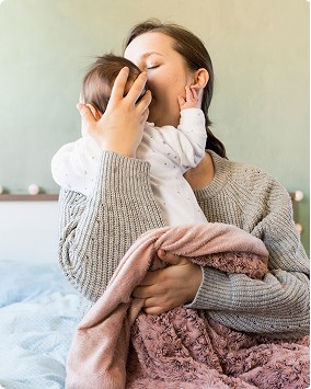 A woman gently cradles a sleeping newborn close to her chest, wrapped snugly in a striped fabric, illustrating tender postpartum care and intimate bonding.