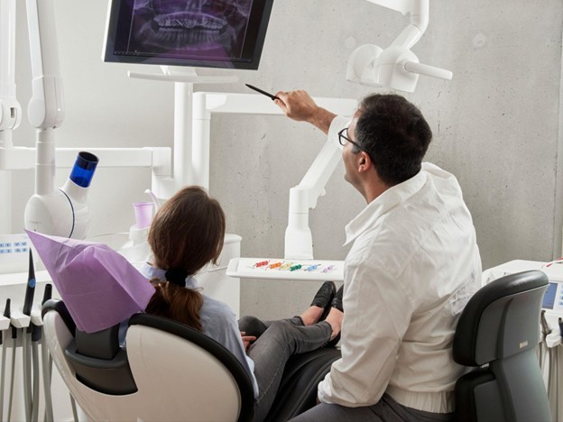 A dentist and patient review a dental X-ray on a monitor in a modern, well-equipped dental office.