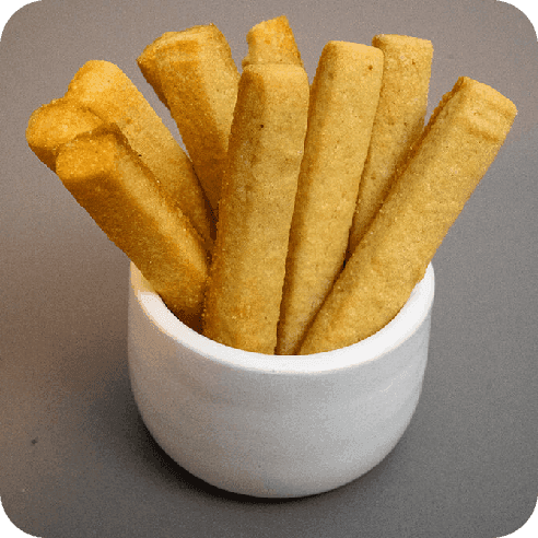 Palitos de galleta de mantequilla dispuestos verticalmente dentro de una taza blanca sobre fondo gris.