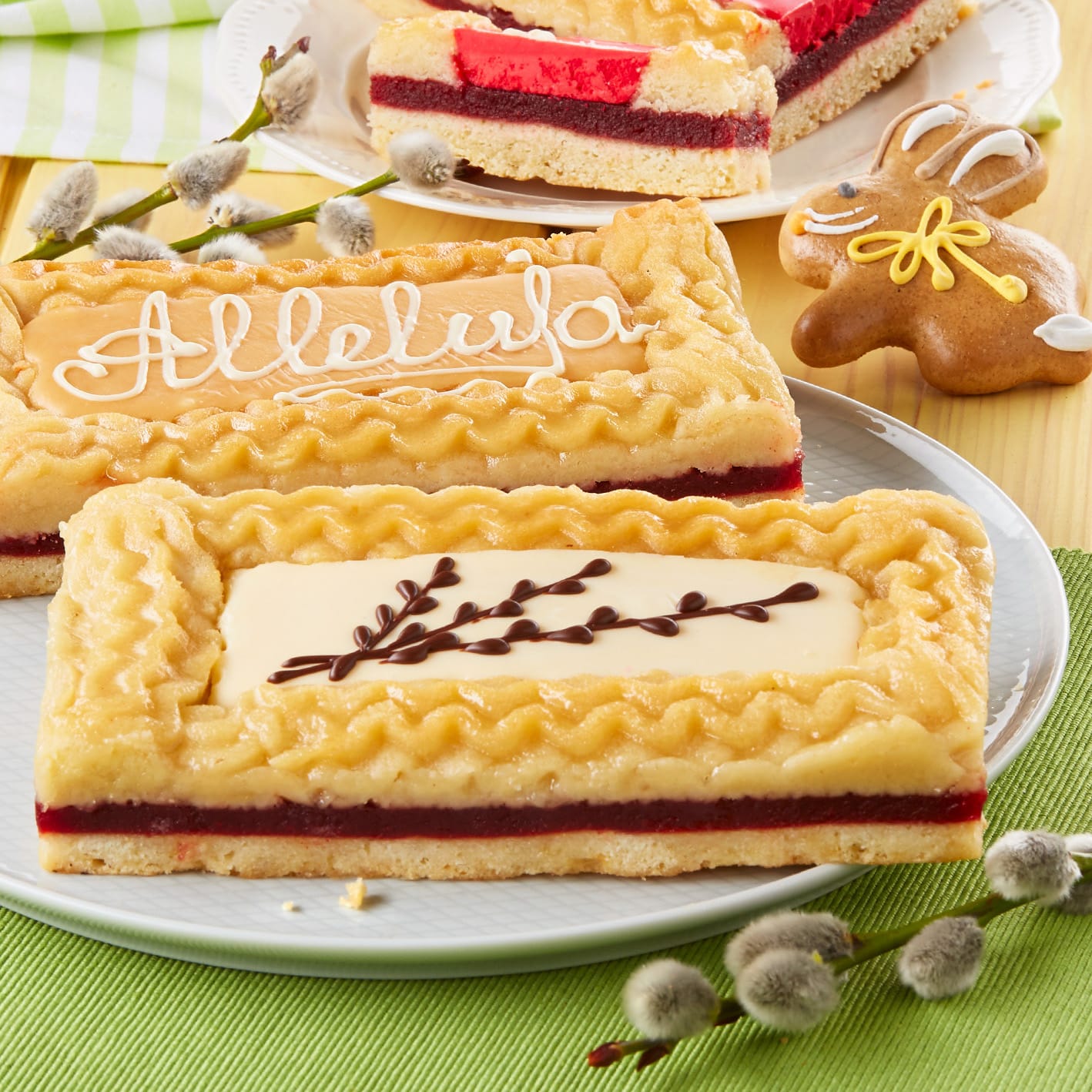 A beautifully arranged food photo session featuring intricately decorated rectangular pastries with a golden crust, topped with delicate white and dark chocolate designs, set on a wooden table adorned with a small gingerbread cookie and sprigs of pussy willow.