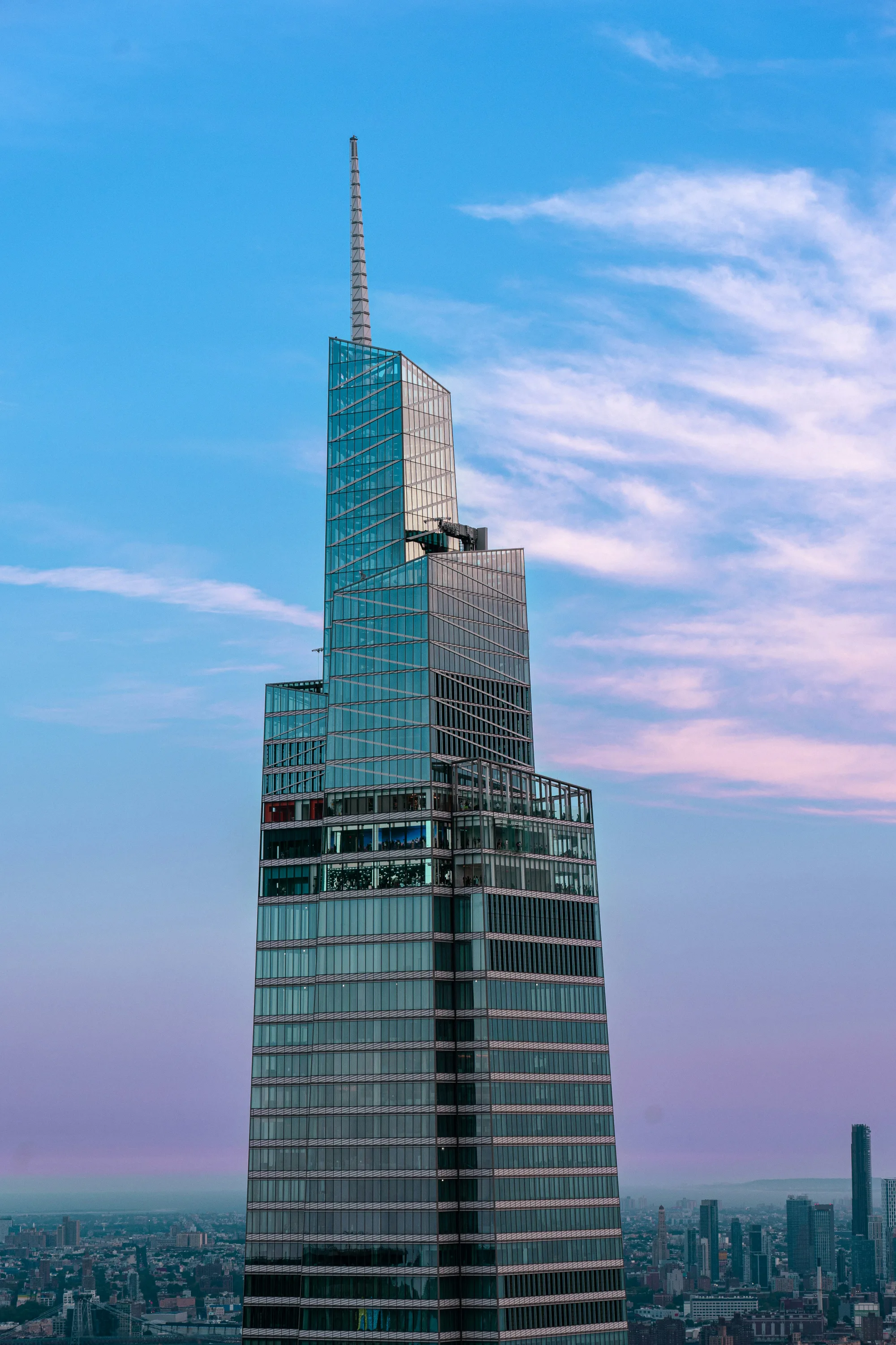 Modern glass skyscraper with antenna against a sunset sky.