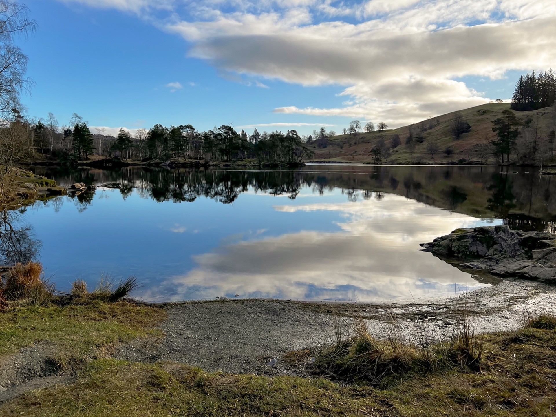 The tarn is still, a mirror reflection of the surrounding trees.