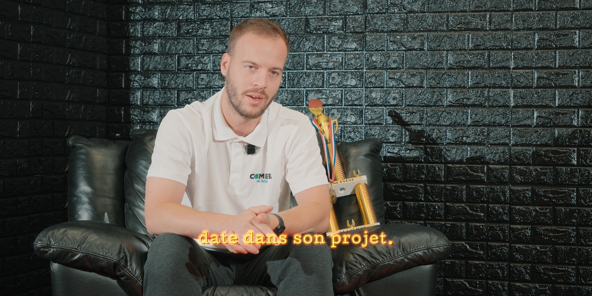 Interview d'un homme assis avec un trophée doré en arrière-plan.