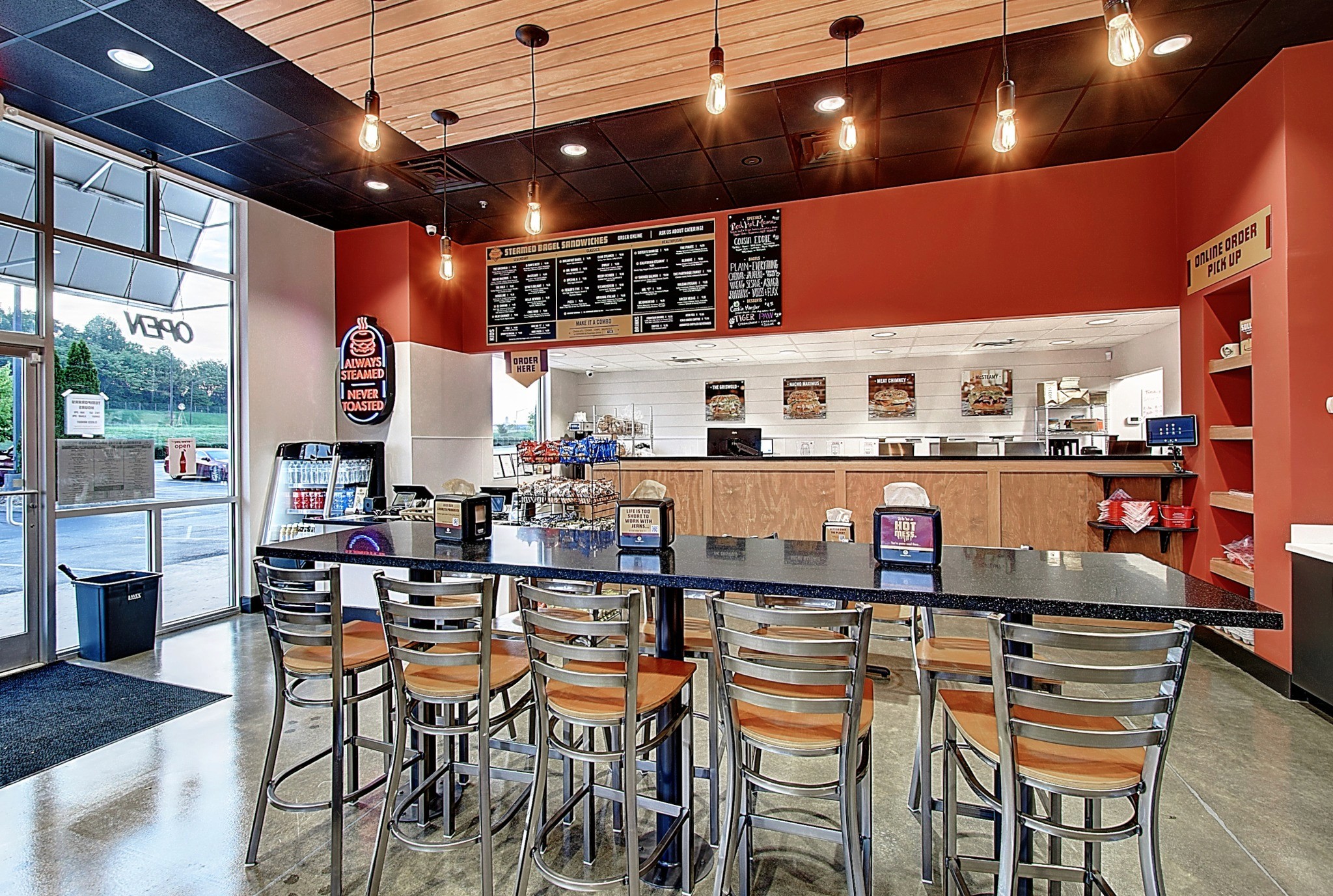 A modern café interior featuring a wooden counter, seating, and warm lighting against red and neutral walls.