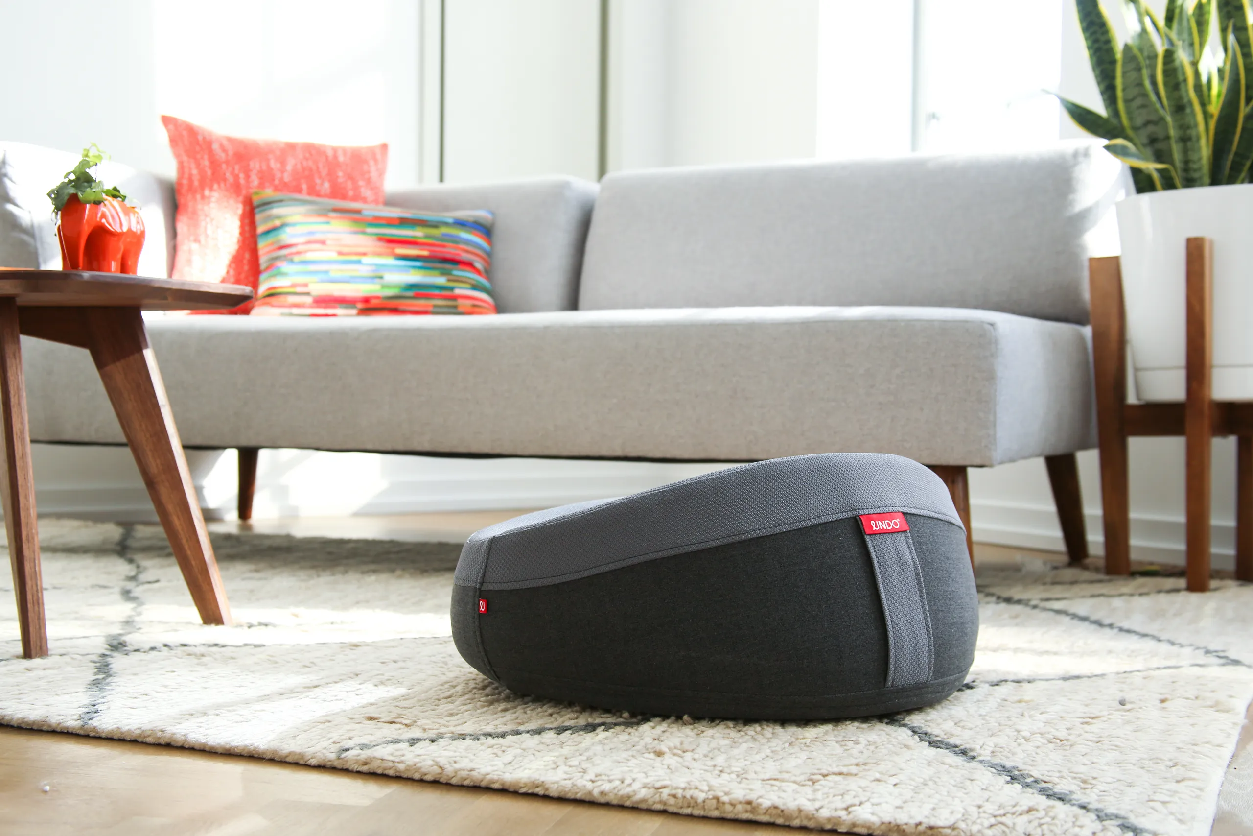 Dark gray UNDO meditation cushion on a rug in a bright modern living room