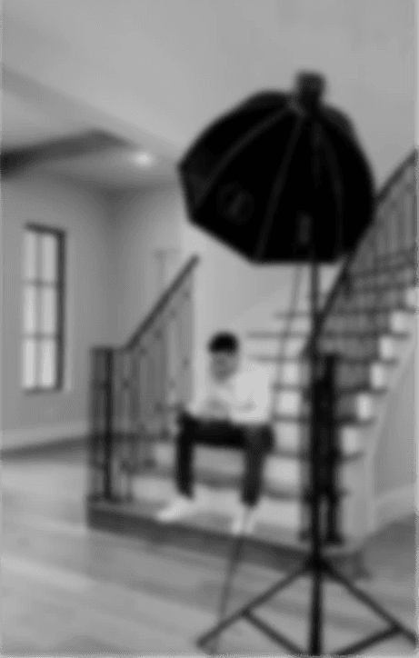 Man sitting in a dimly lit room, wearing a beige shirt and looking contemplative.