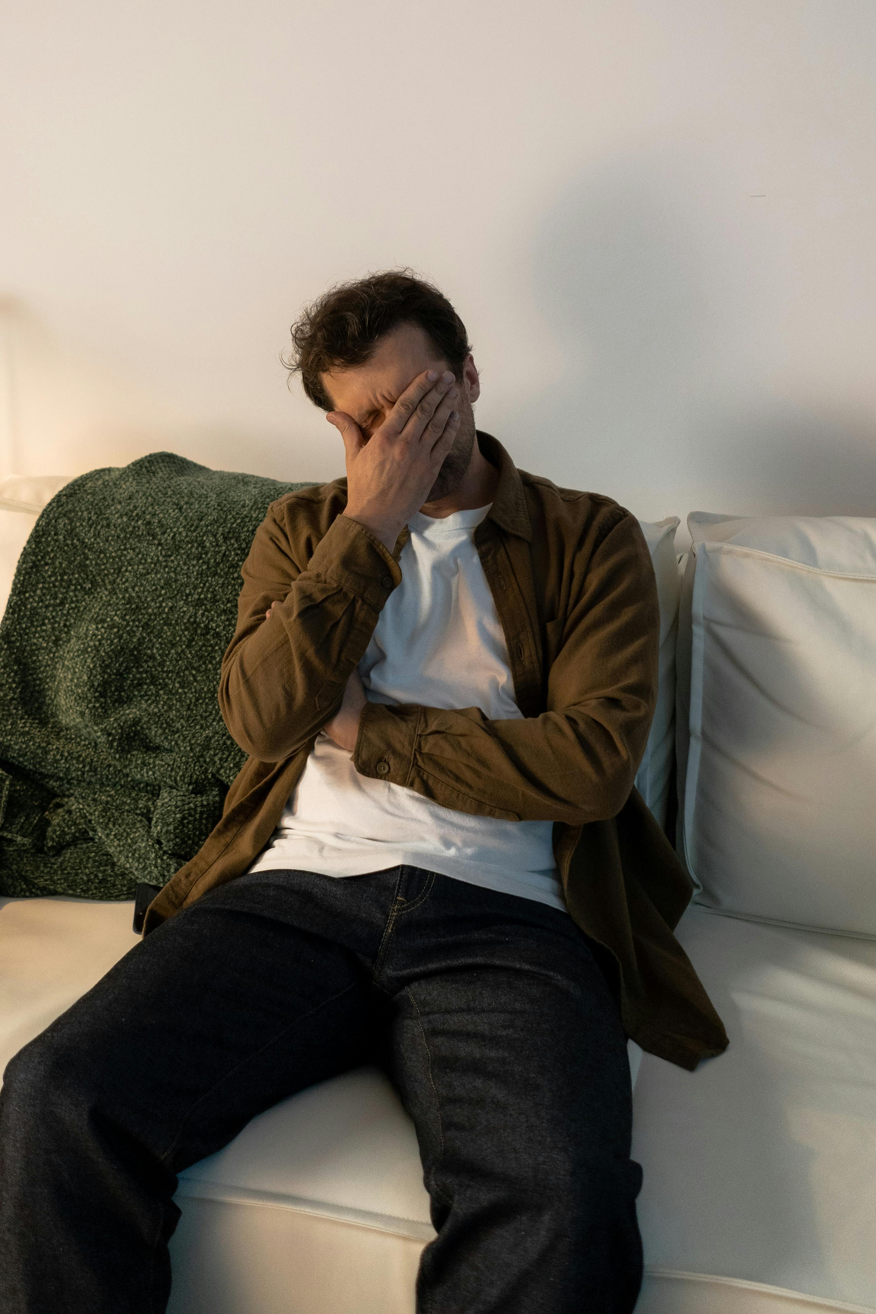 Uomo sul divano con mano sul viso: stress e stanchezza, bisogno di aiuto psicologico