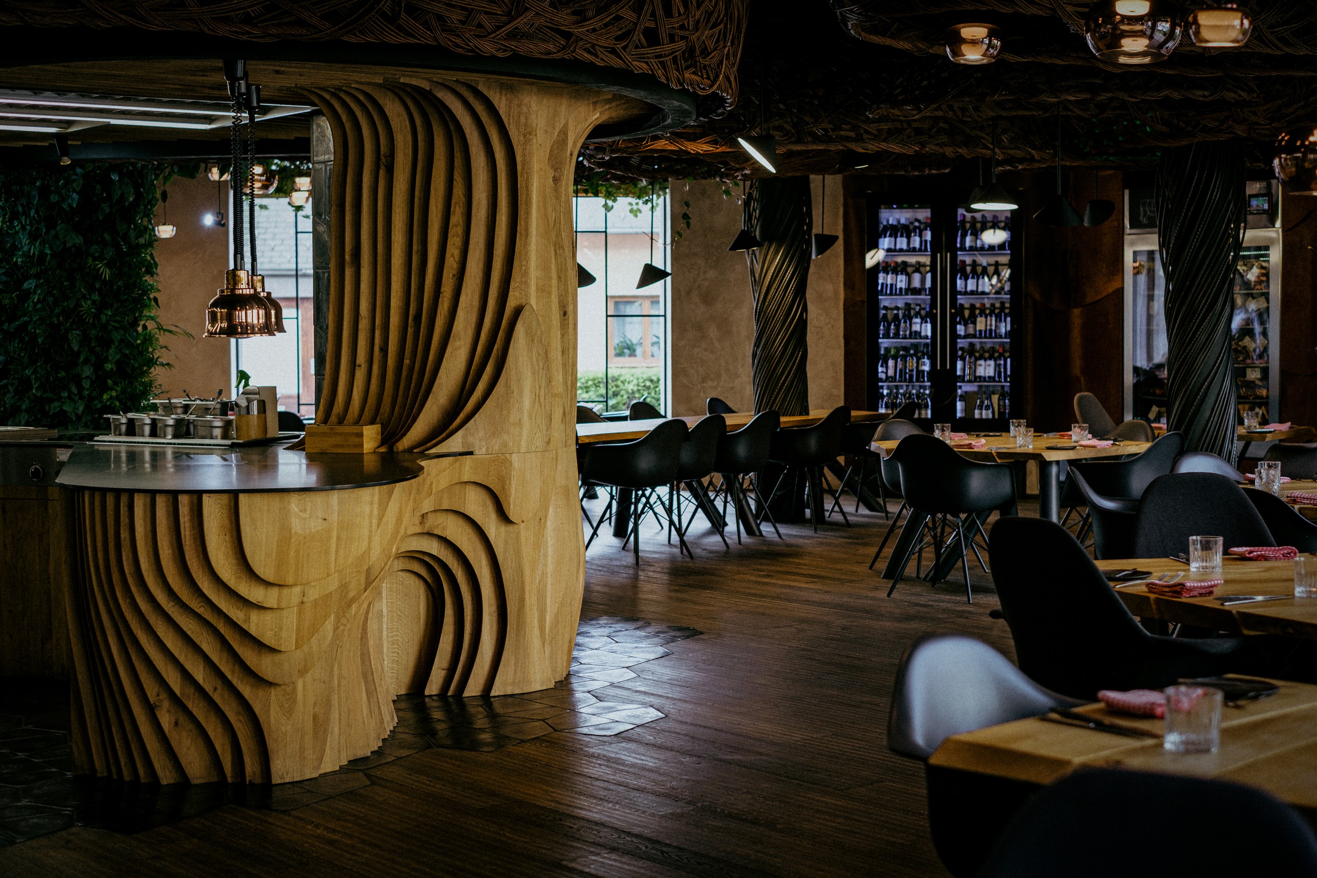 Moderní designový interiér Steak Restaurant Olomouc s organickými dřevěnými prvky, tlumeným osvětlením a vinnou vitrínou v pozadí