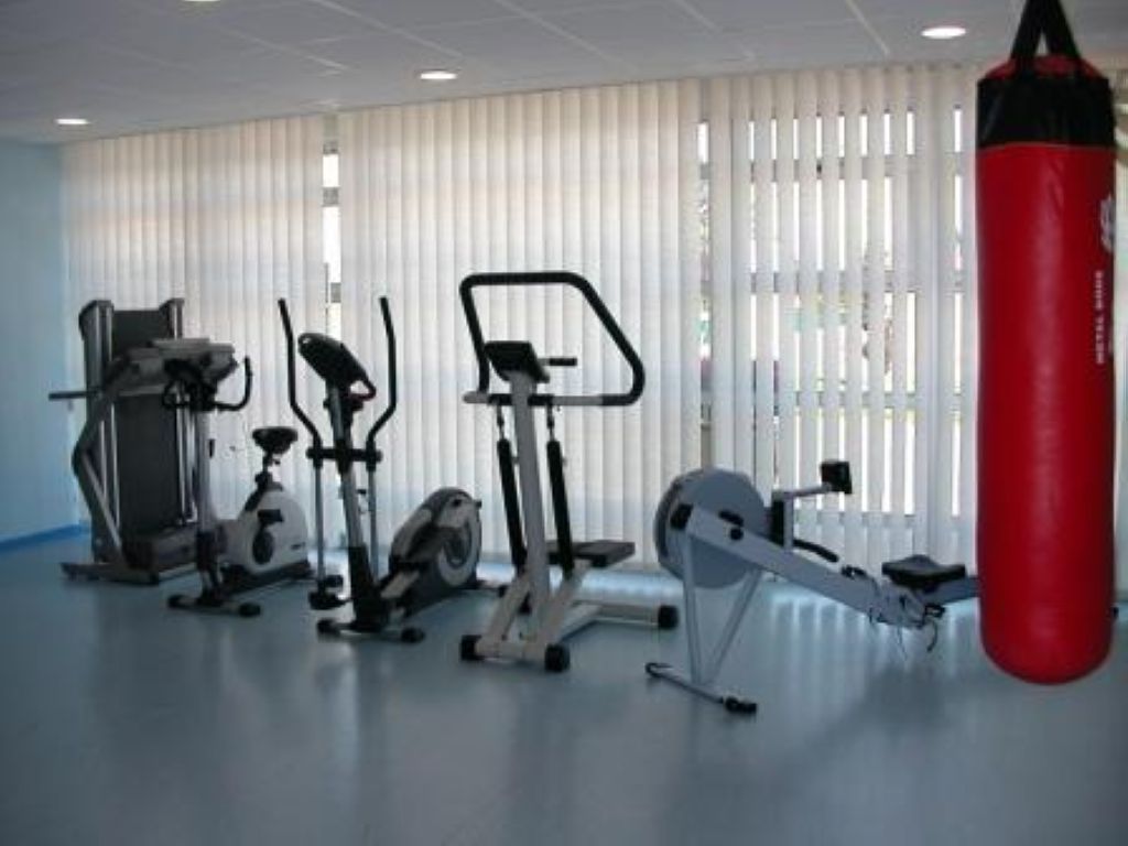 Fitness and rehabilitation room with exercise bikes, training equipment, red punching bag, and bright natural lighting
