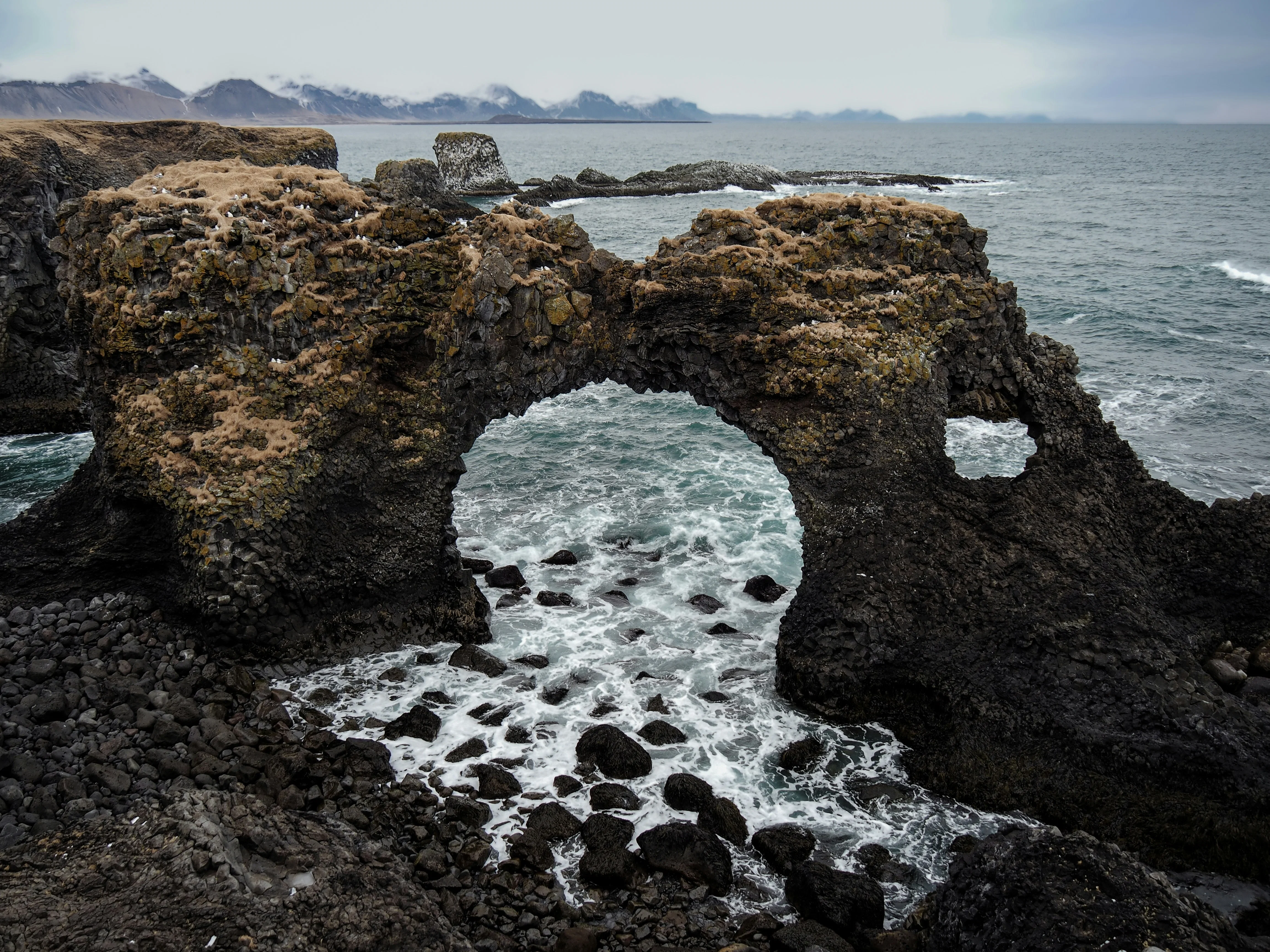 A natural stone arch formed from dark basalt rocks standing in the ocean near the coast.